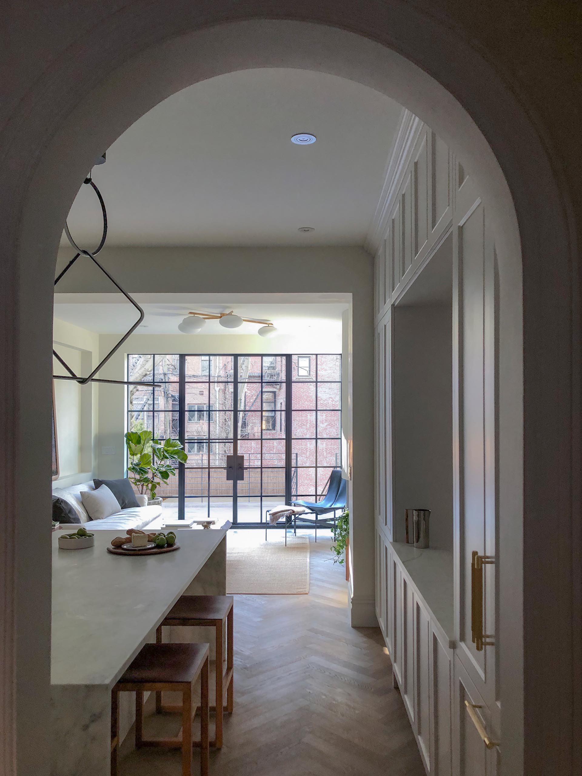 A contemporary interior with a white kitchen and black-framed steel doors and windows.