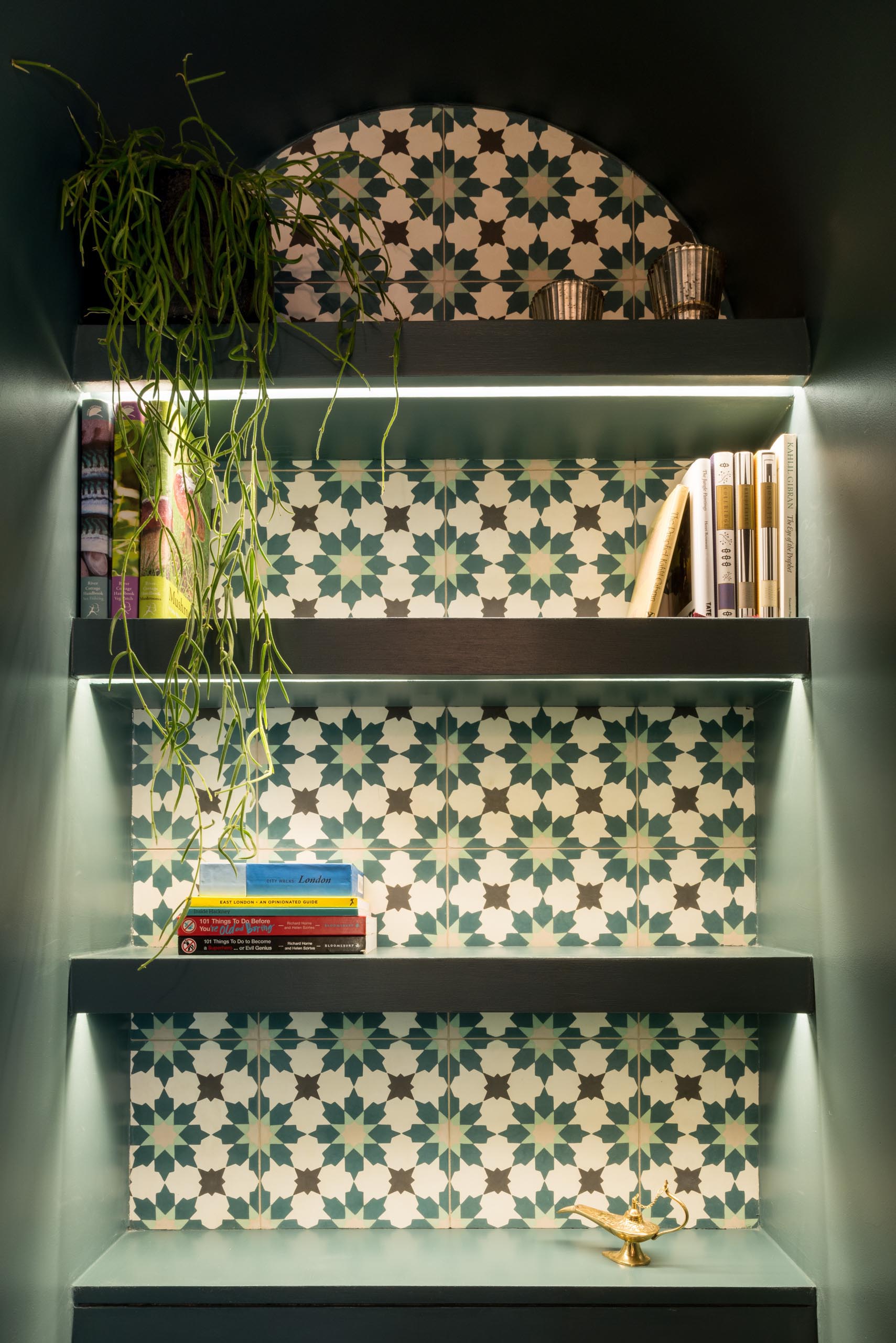 A powder room with a shelving niche lined with patterned tile, and hidden lighting.