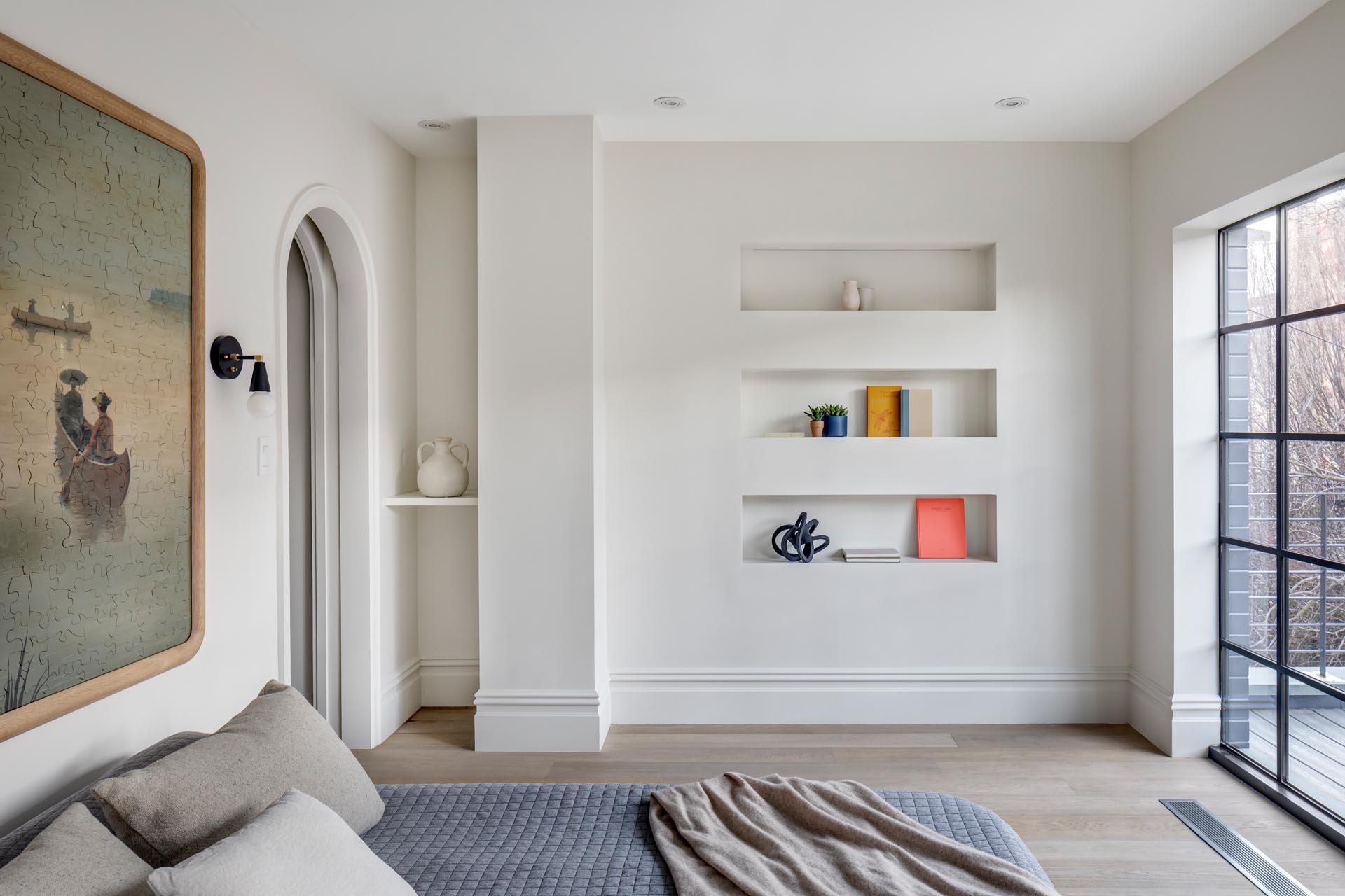 A modern master bedroom with built-in shelving niches, and an arched doorway.