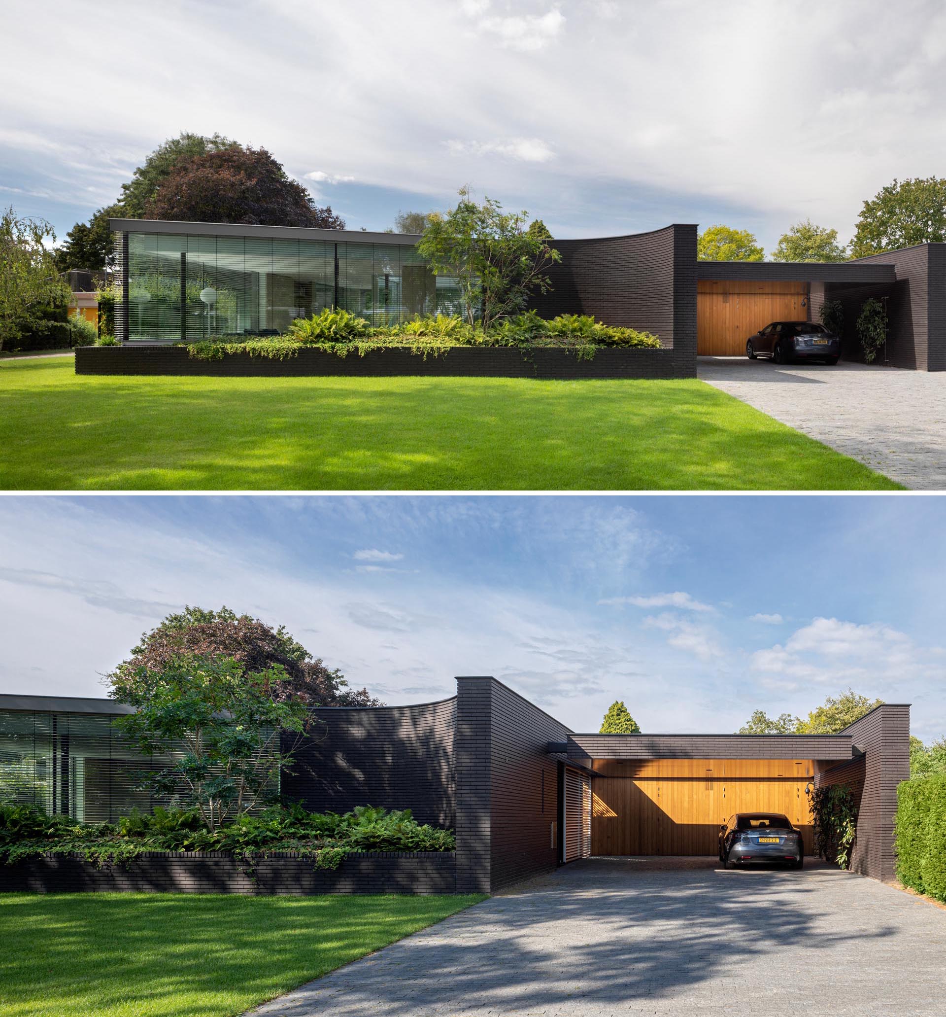 The black brick facade of this modern home features curves and has large integrated planters that highlight the lush greenery.