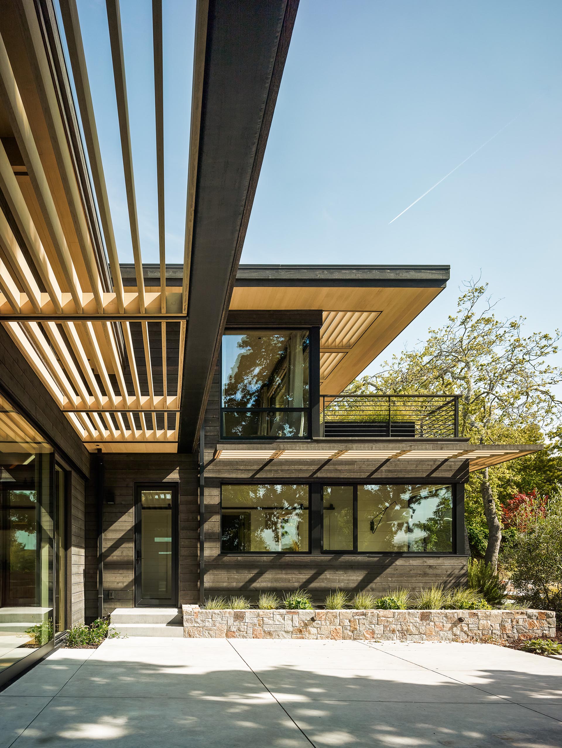 A modern house exterior with black-stained cedar siding and light wood sunscreens.