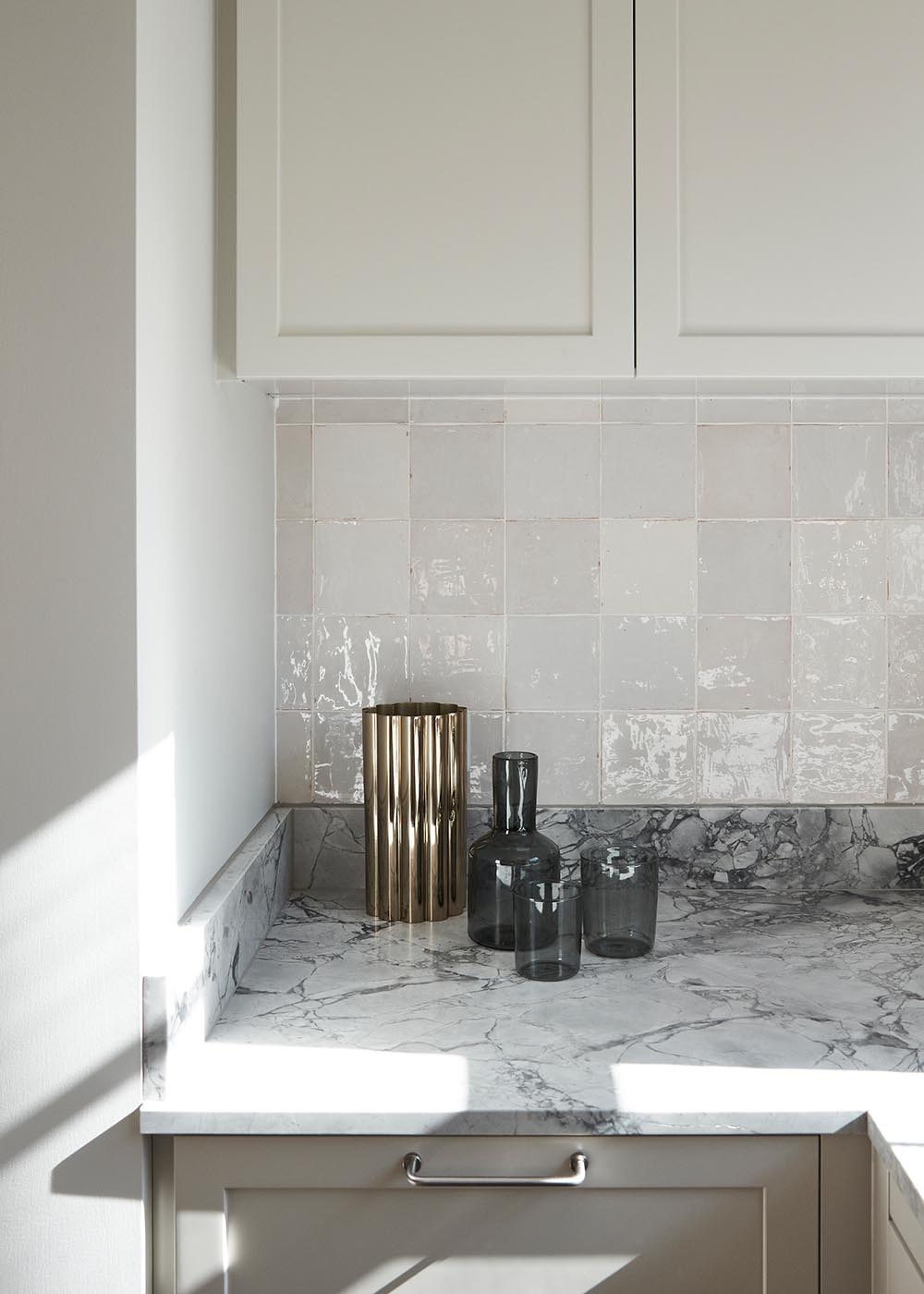 A contemporary kitchen with stone counters, warm textures, handmade tiles, and pale toned cabinetry.