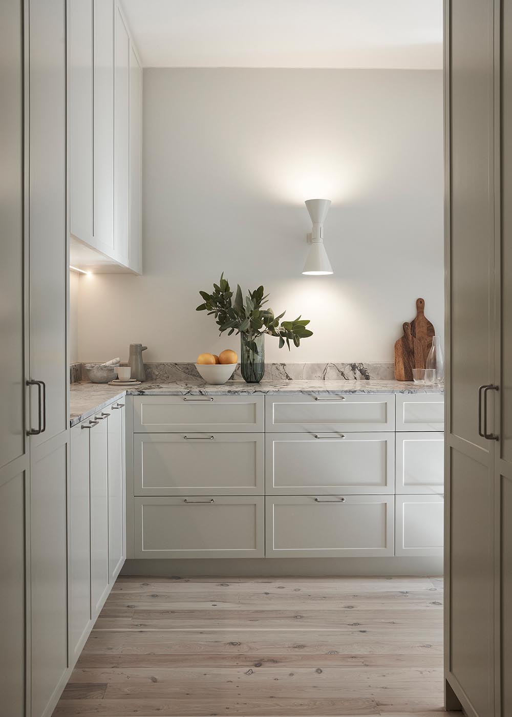 This modern kitchen was designed to offer an abundance of storage and surface space. Stone counters, warm textures, and pale toned cabinetry complement the other design choices throughout the apartment.