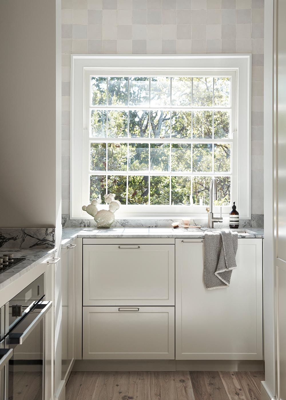 A kitchen with stone counters, warm textures, handmade tiles, and pale toned cabinetry.