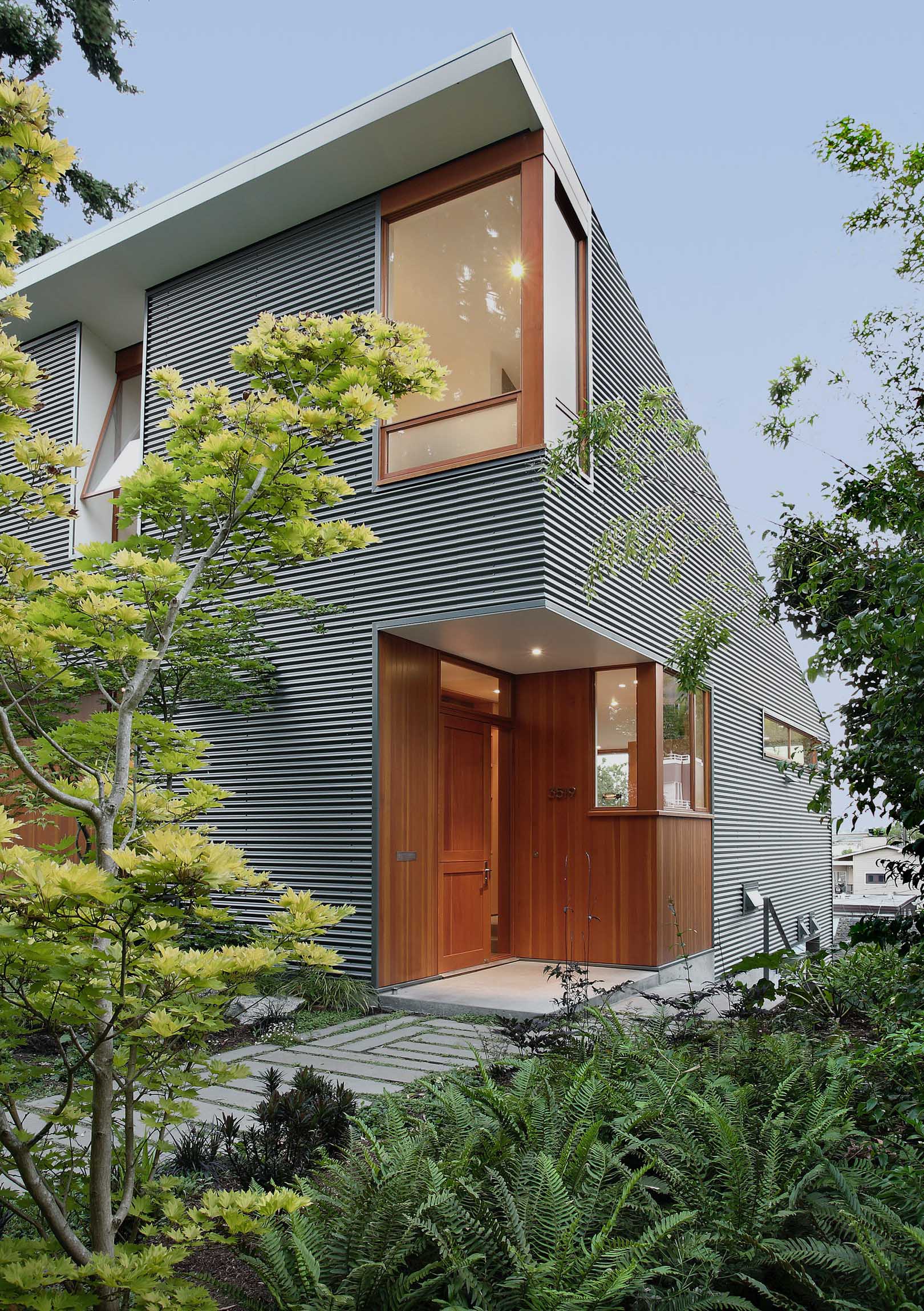A modern house with corrugated metal siding and a wood front door and window frames.