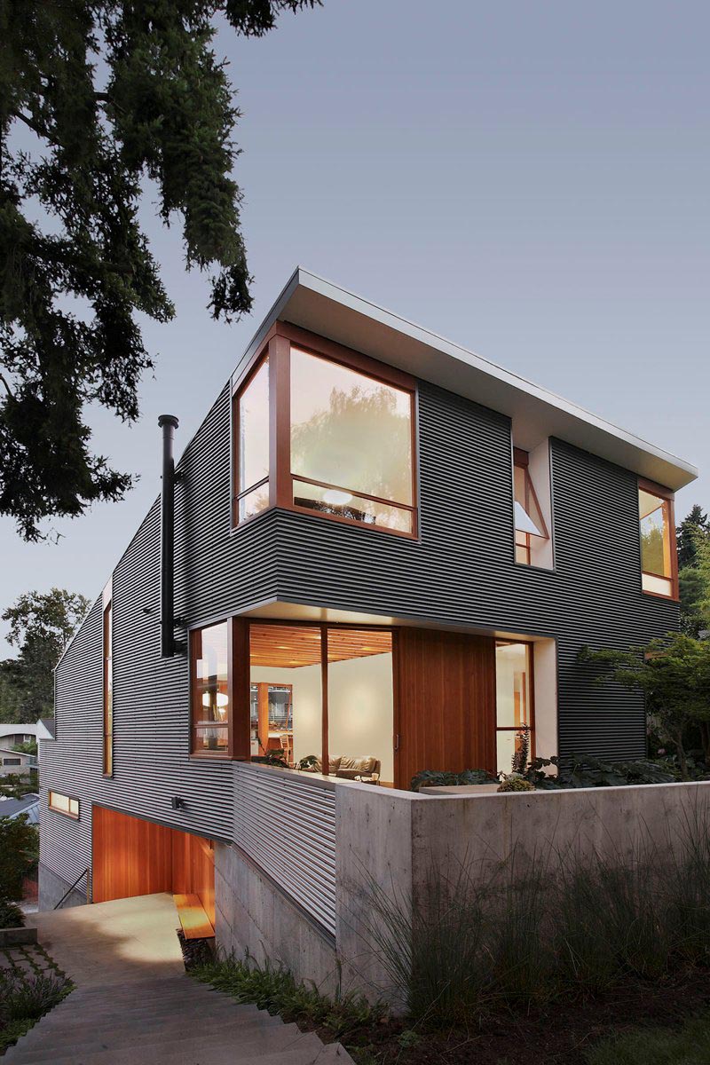A modern house with corrugated metal siding, concrete elements, and wood window frames.
