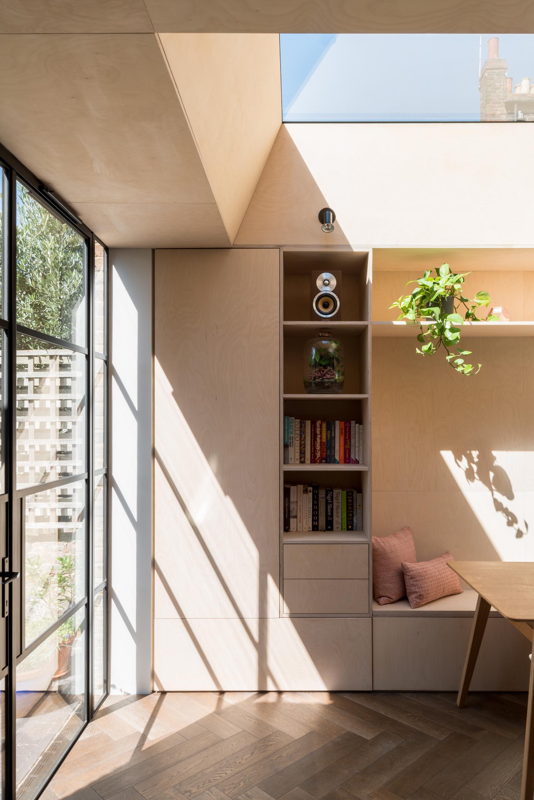 A new dining room has been designed with fitted storage, a long bespoke dining bench, plywood walls, Crittall doors, and two skylights.