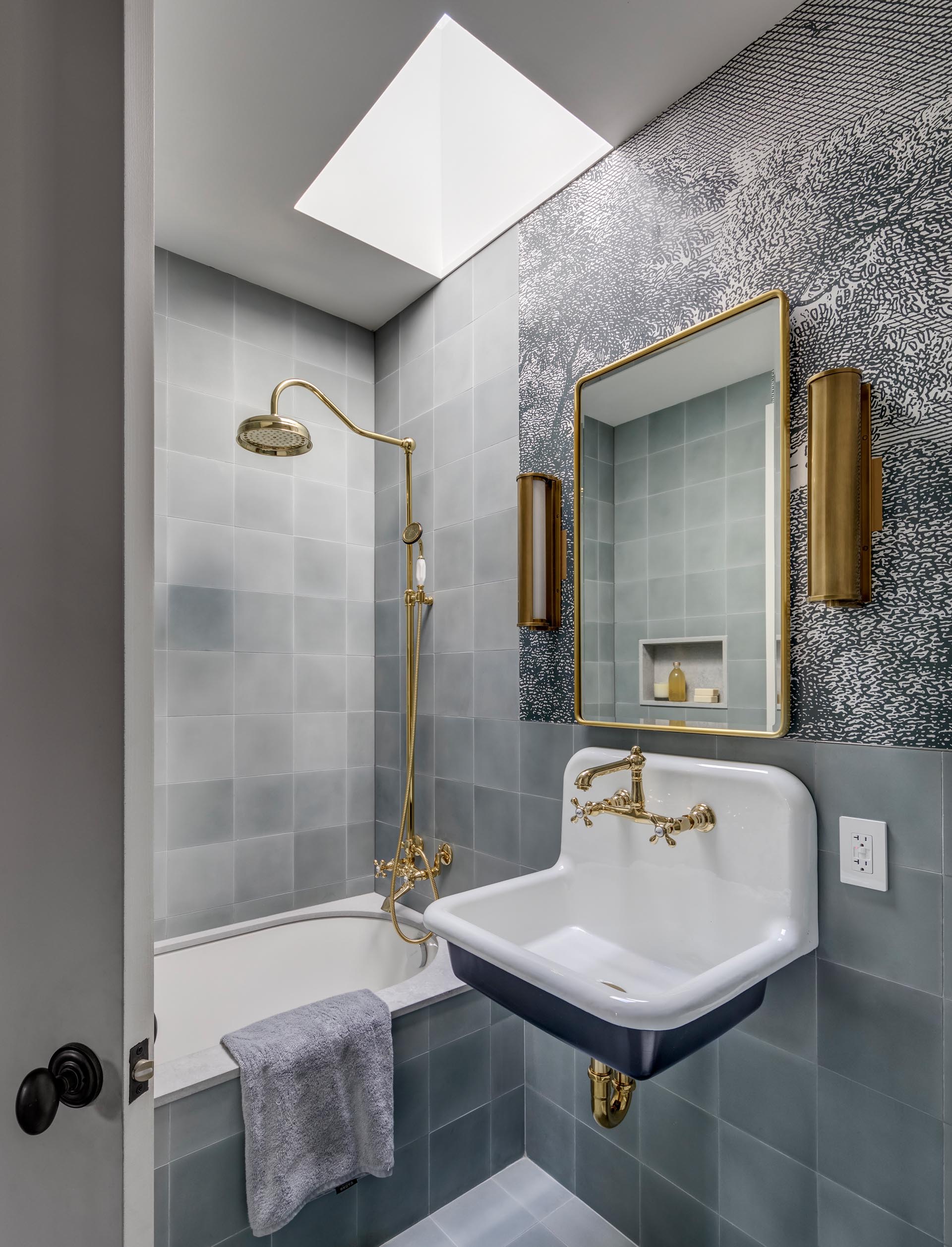 A bathroom with a floating vanity, gold hardware and faucet, and grey tiled walls and bathtub surround.