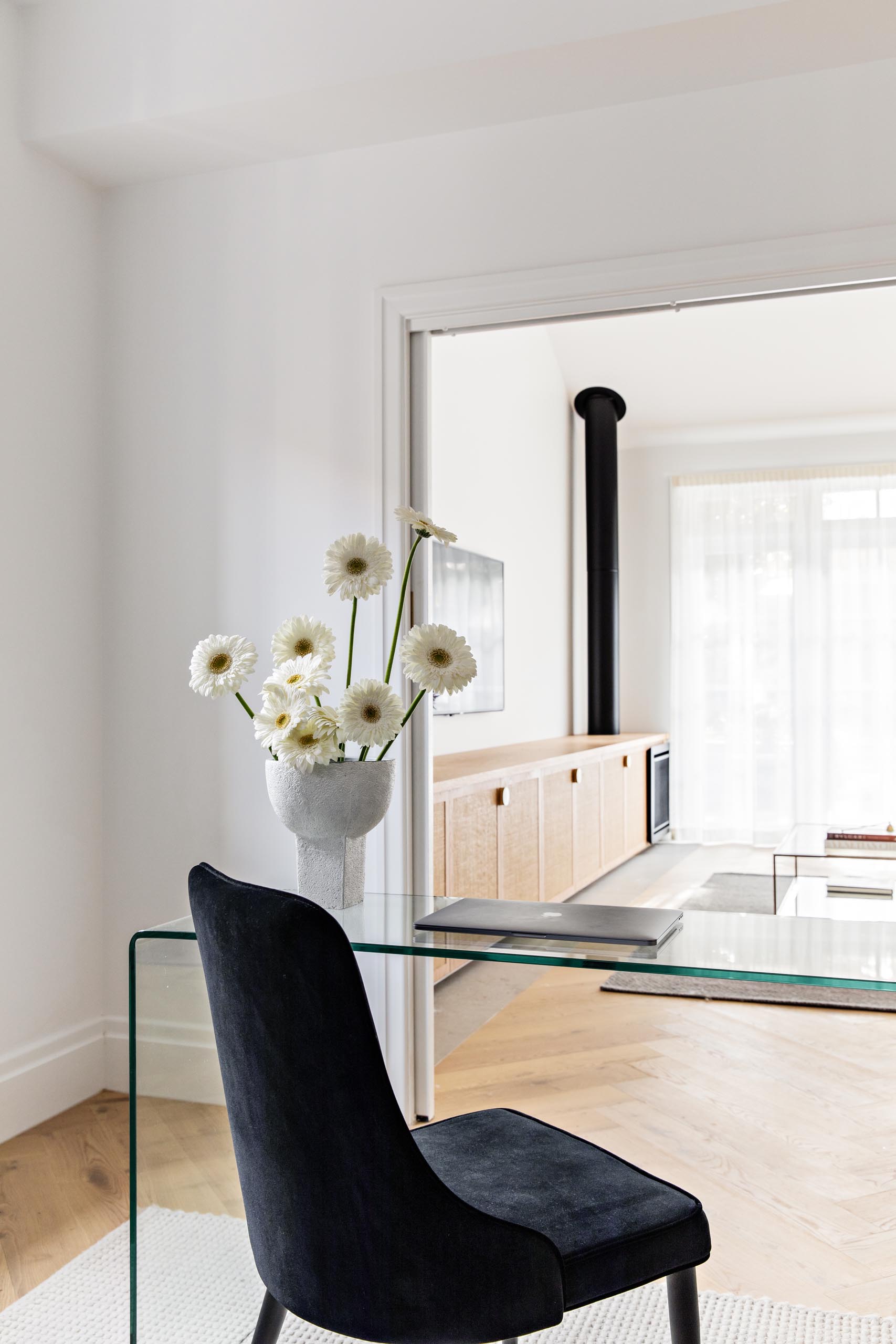 A modern home office with a glass desk, and an black upholstered chair.