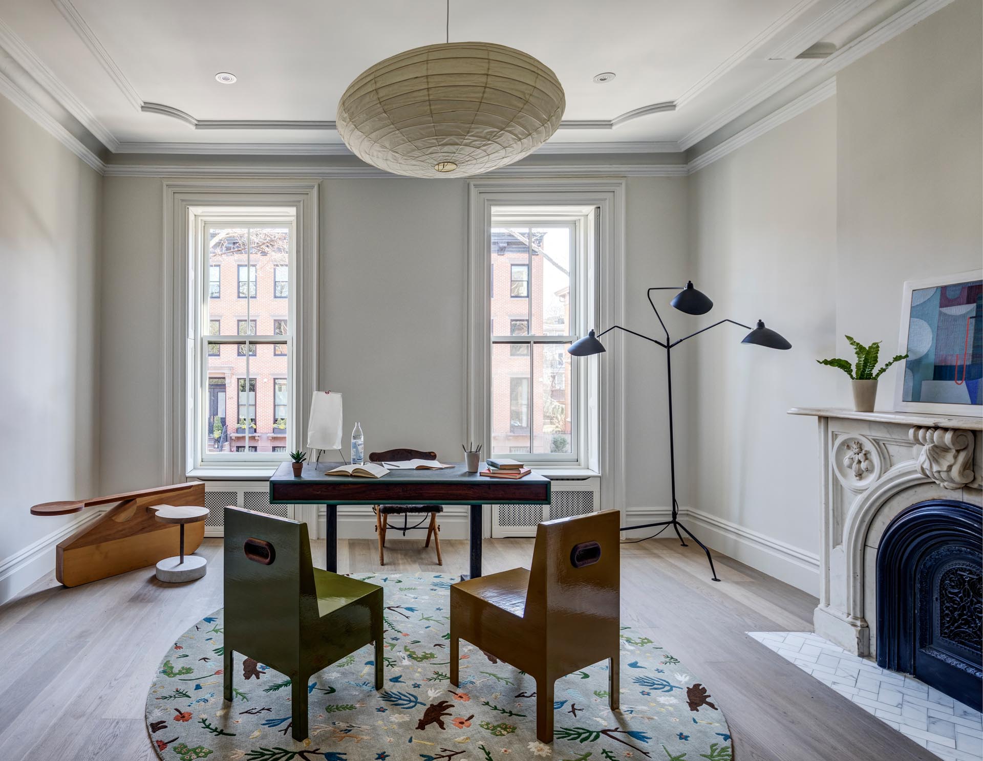 A home office with tall windows and an arched fireplace that includes a tiled hearth.