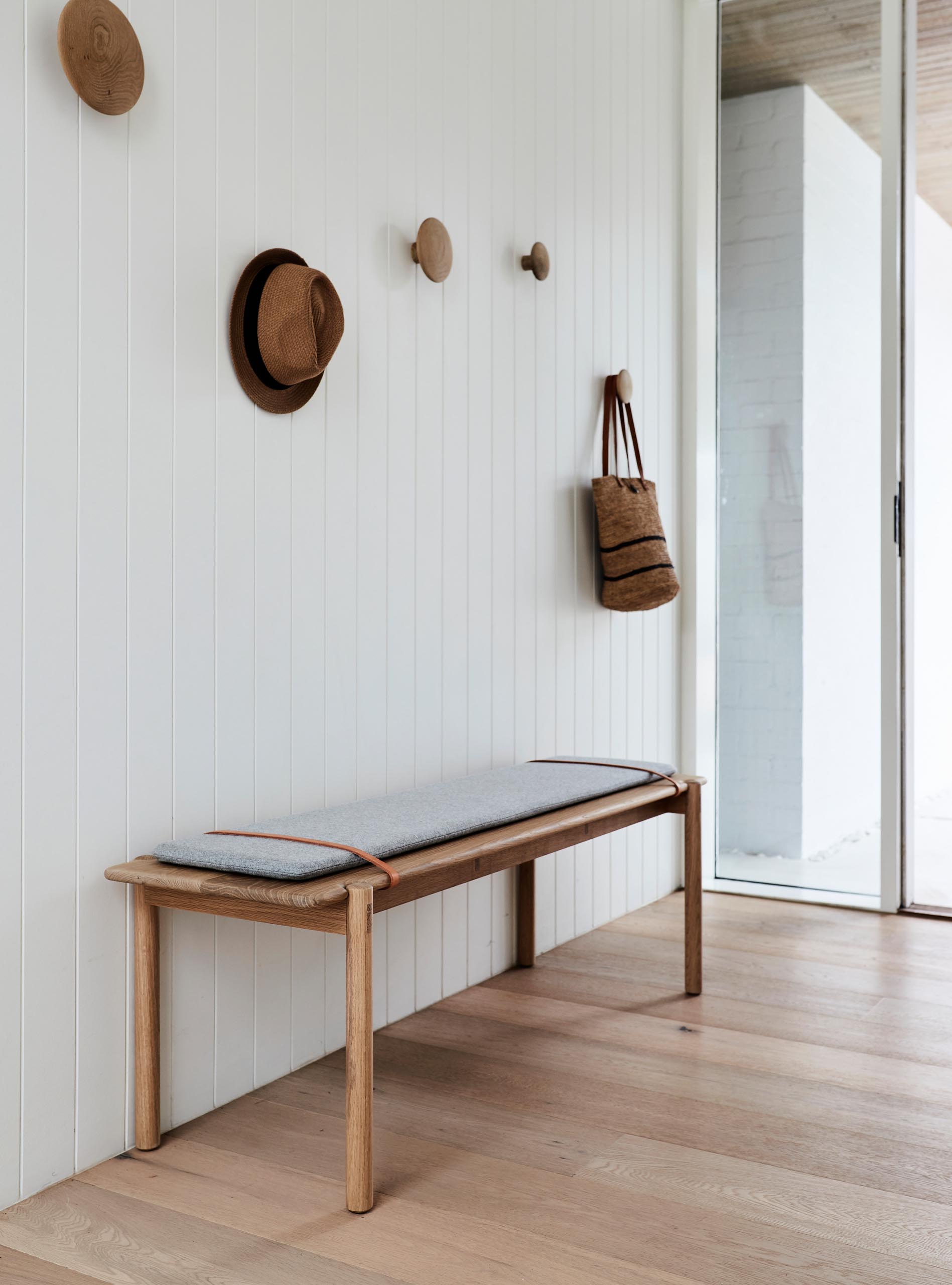 This modern entryway has a white wall, oak floors, a simple bench, and round wood wall hooks.