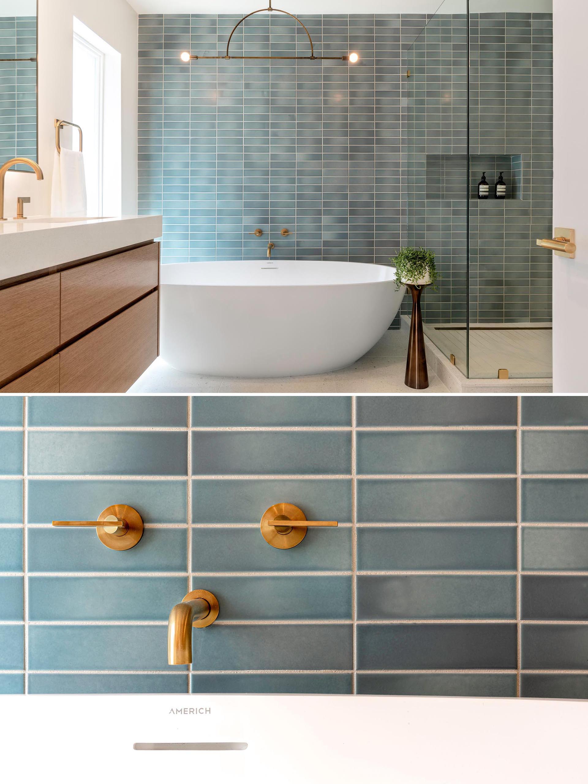 This modern bathroom with blue rectangular wall tile, a minimalist light fixture, a freestanding white bathtub, and brass fixtures.