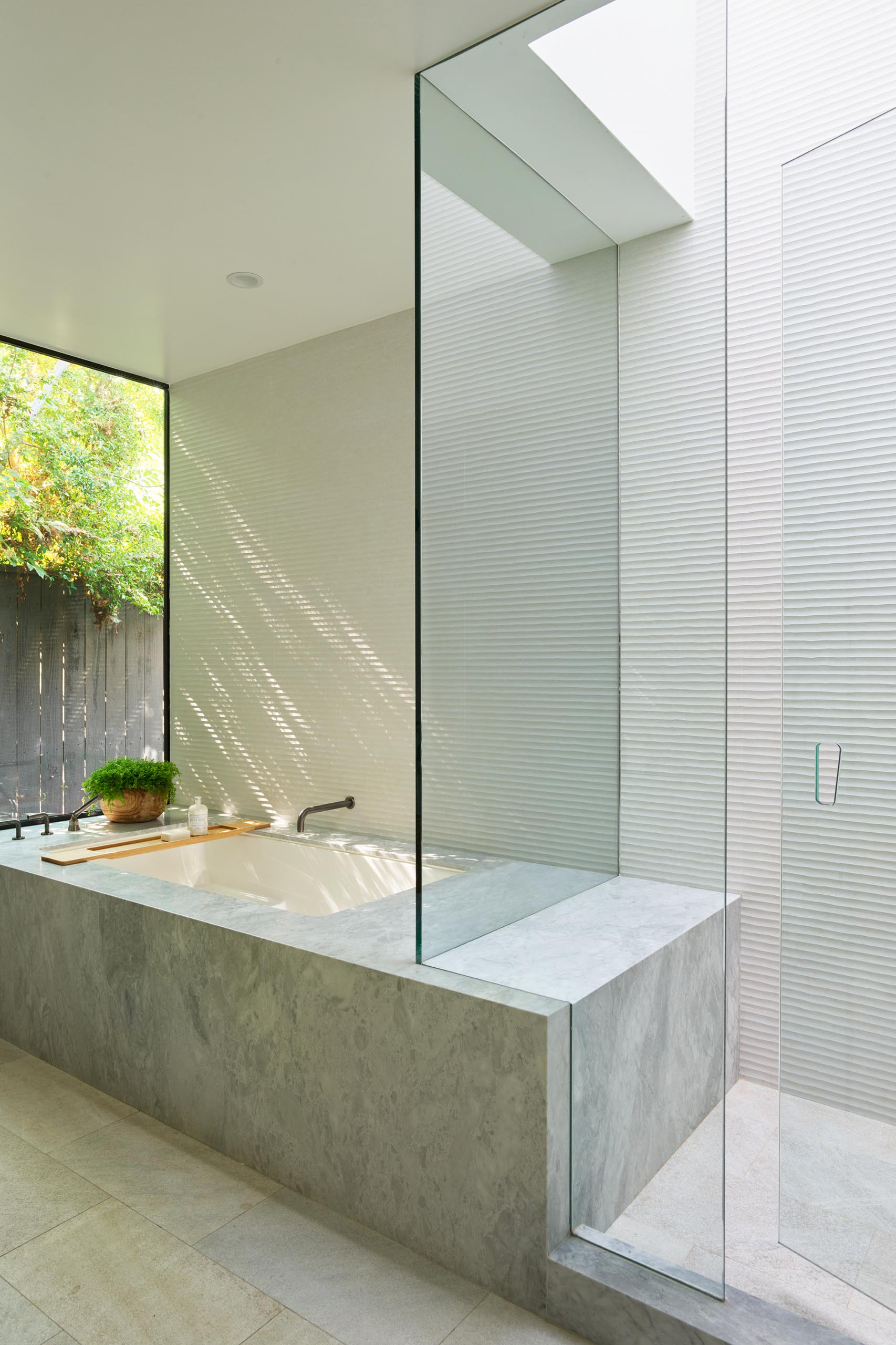 A modern bathroom with a walk-in shower and a built-in bathtub with views of plants outside.