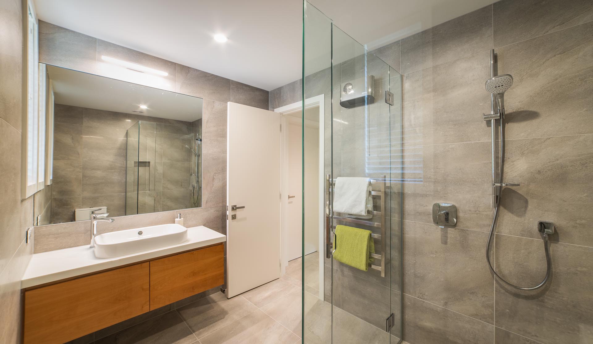 A modern bathroom with large format tiles, a wood vanity, and a white countertop with matching sink.