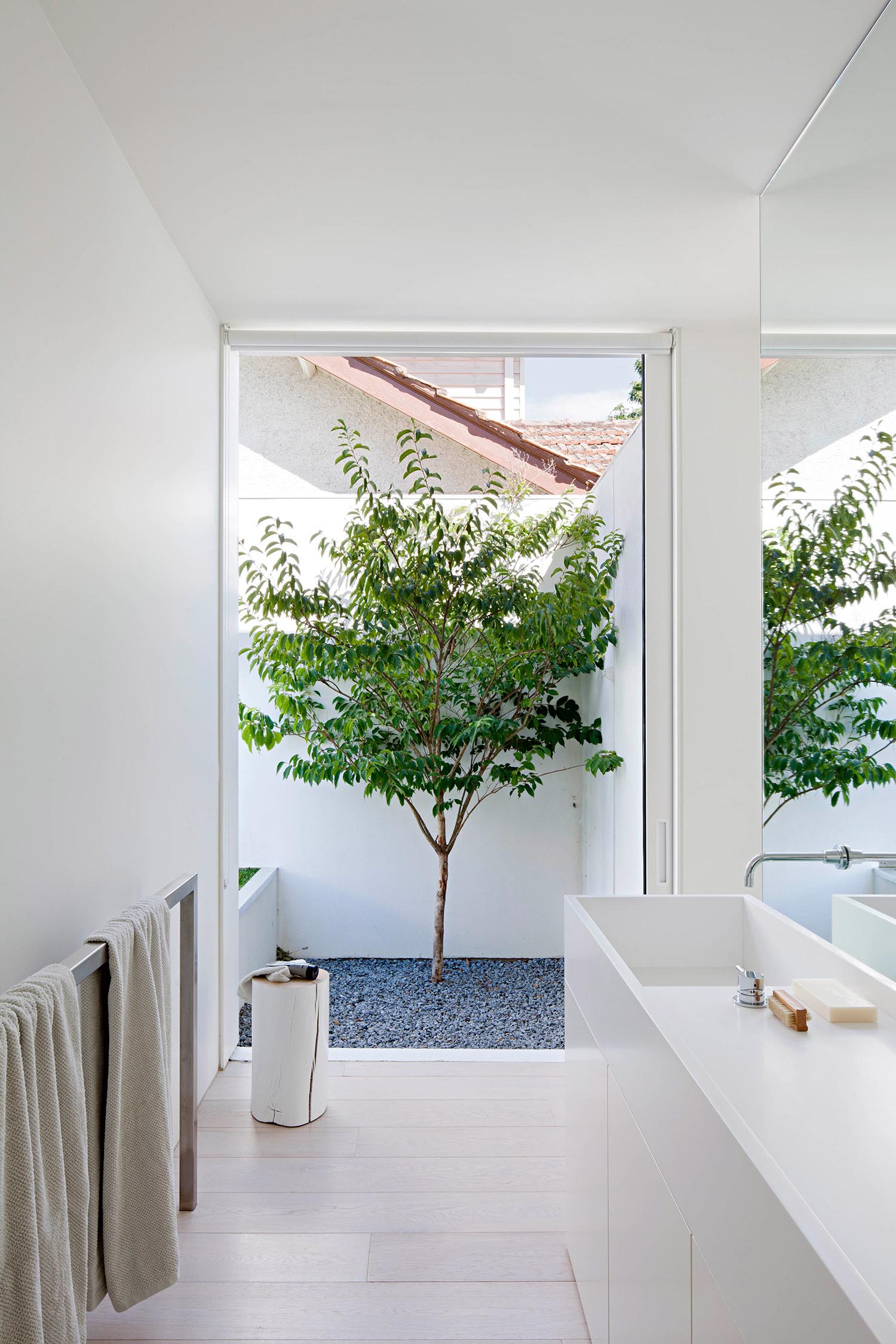 A modern white bathroom with a large window, minimalist white vanity, and metal towel rack.