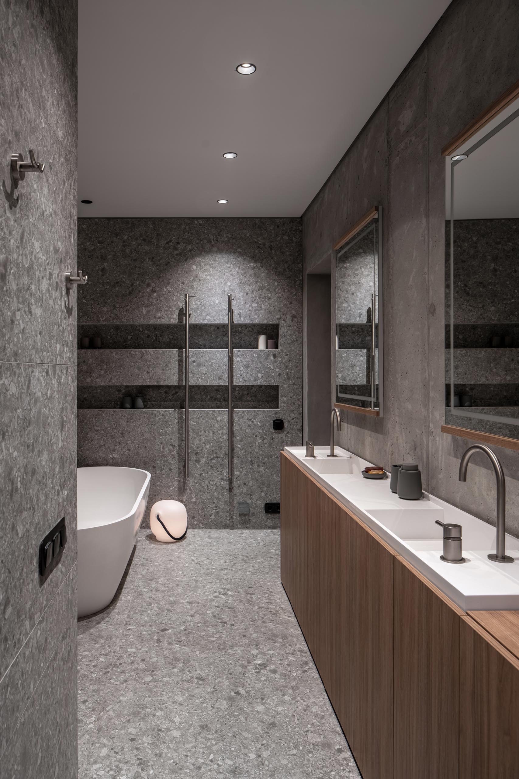 A modern bathroom with a narrow custom-made double sink vanity, a freestanding white bathtub, and a shower with built-in shower niches.