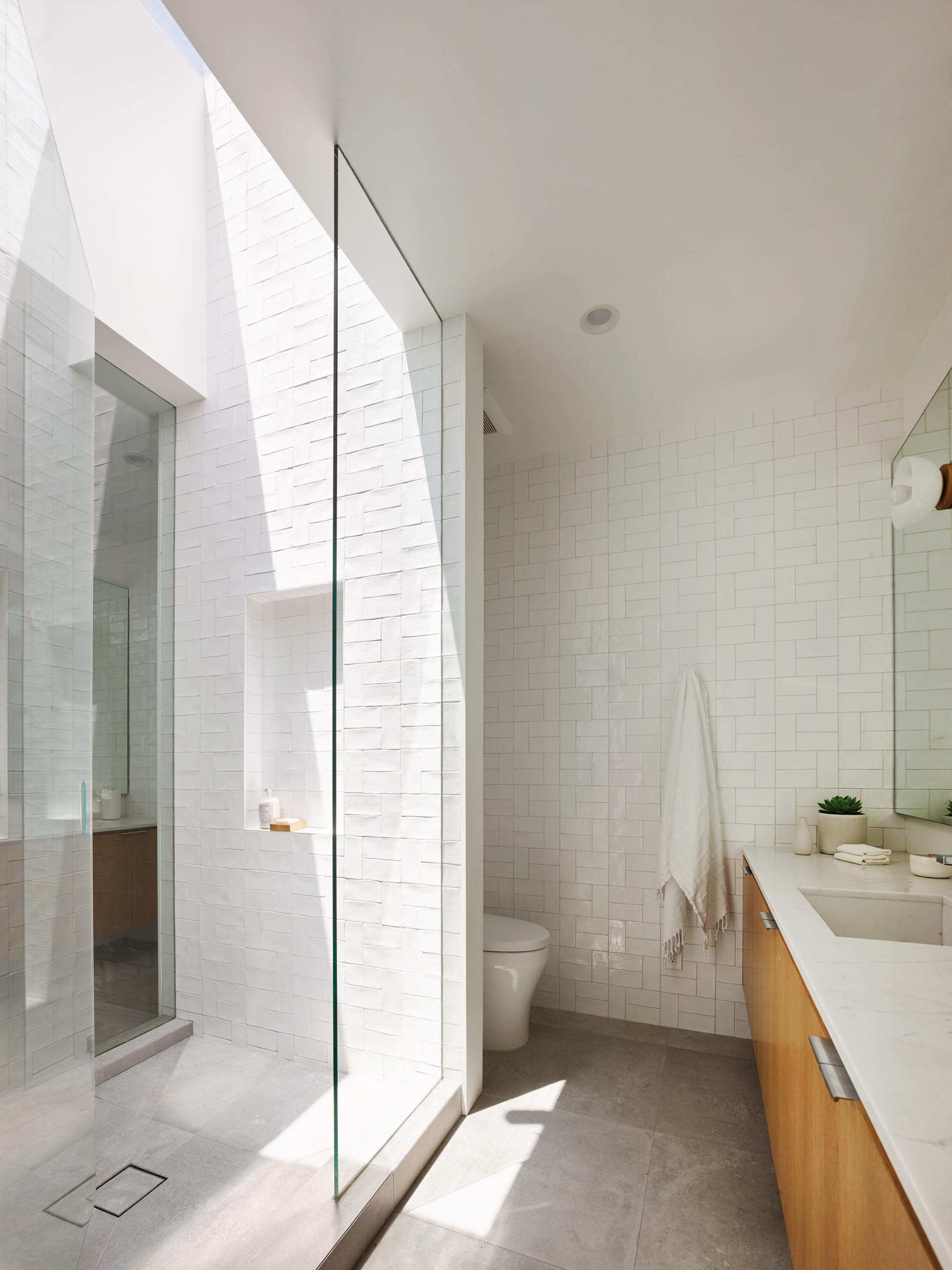 A modern bathroom with a walk-in shower with white tiles and a skylight, that adds plenty of natural light.