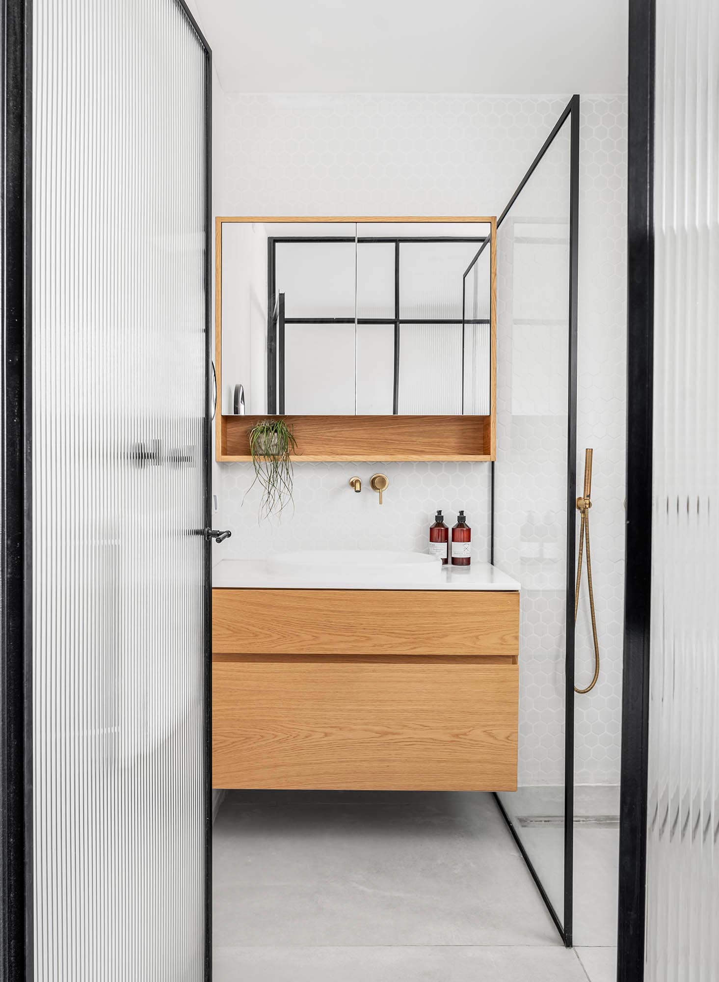 Inside this modern bathroom is a floating wood vanity with a white countertop and sink, while white hexagonal tiles cover the walls. 