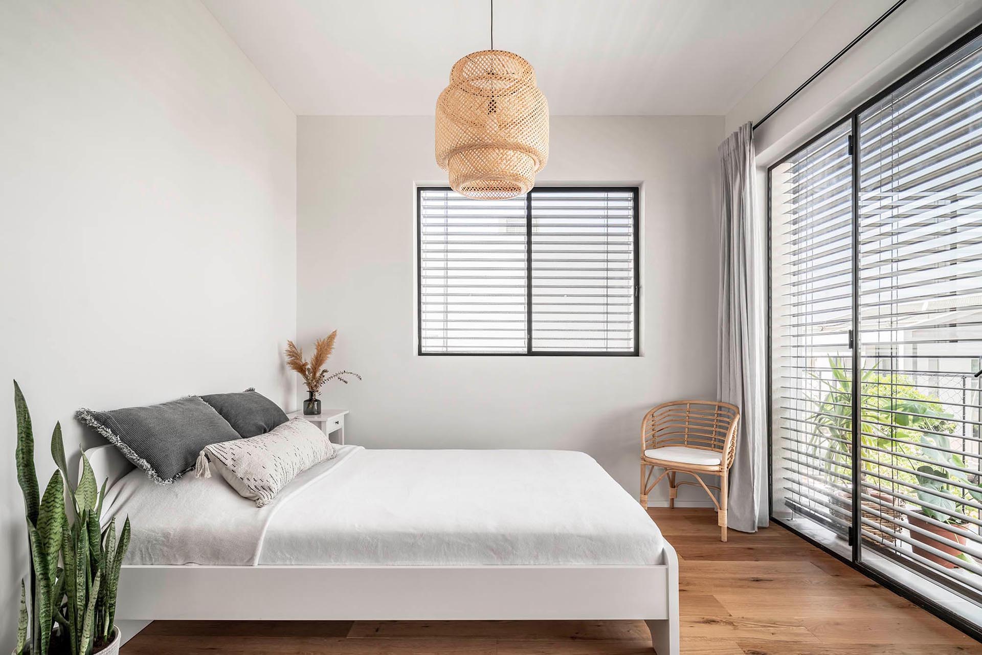 This modern bedroom is simple and bright with light-colored walls, wooden accents, and plants.