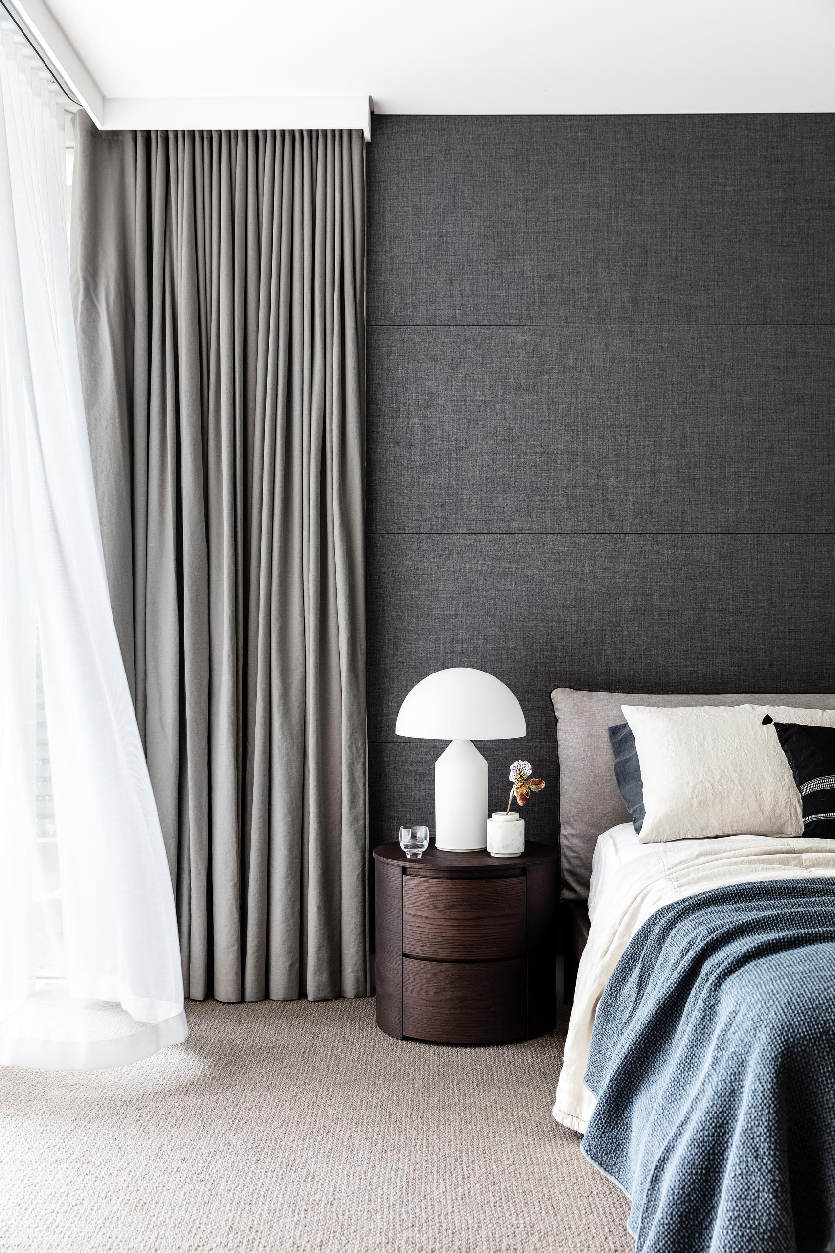 In this master bedroom, a charcoal wall and grey curtains create a bold accent for the space. 