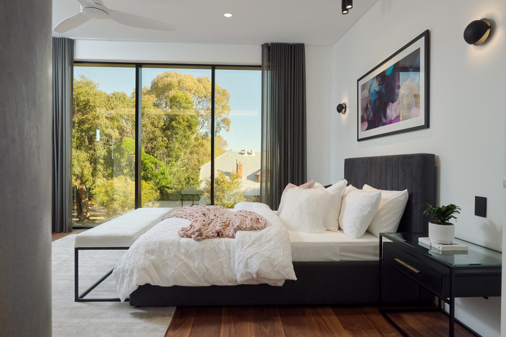 A modern master bedroom with rich wood floors that add a sense of warmth, while an upholstered grey bed frame complements the floor-to-ceiling grey curtains.