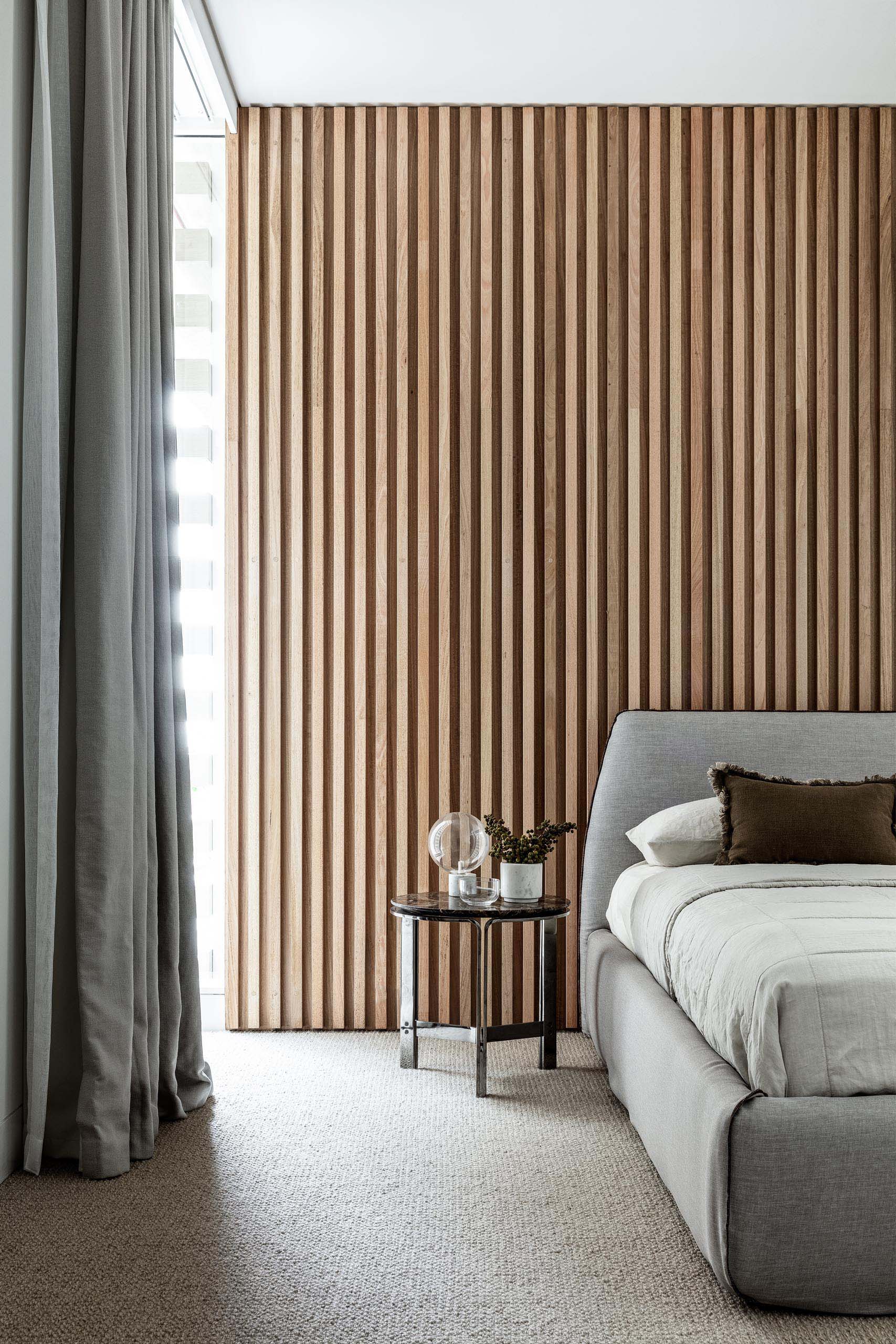 In this modern bedroom, a wood slat wall has been used to create an accent wall behind the grey upholstered bed.