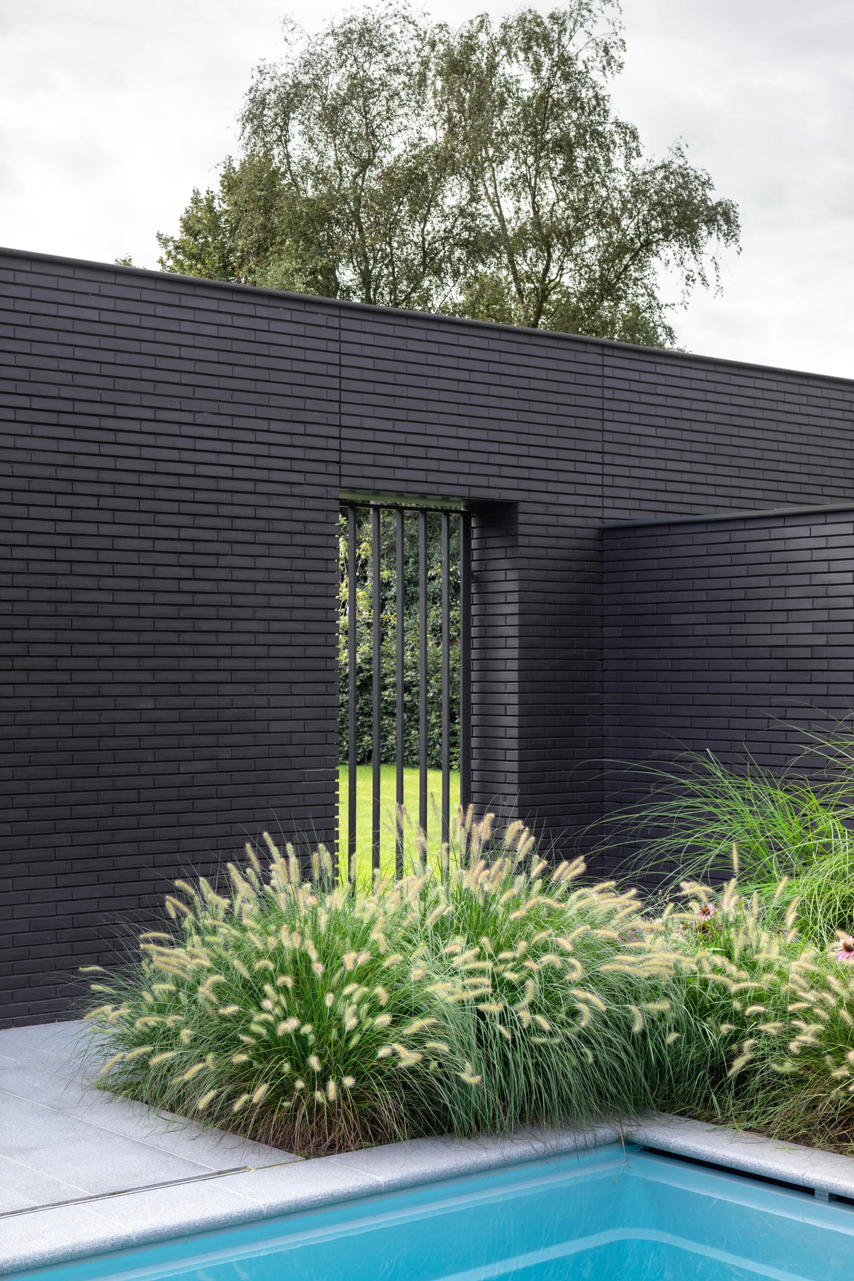 A black brick home exterior with lush gardens and a swimming pool.