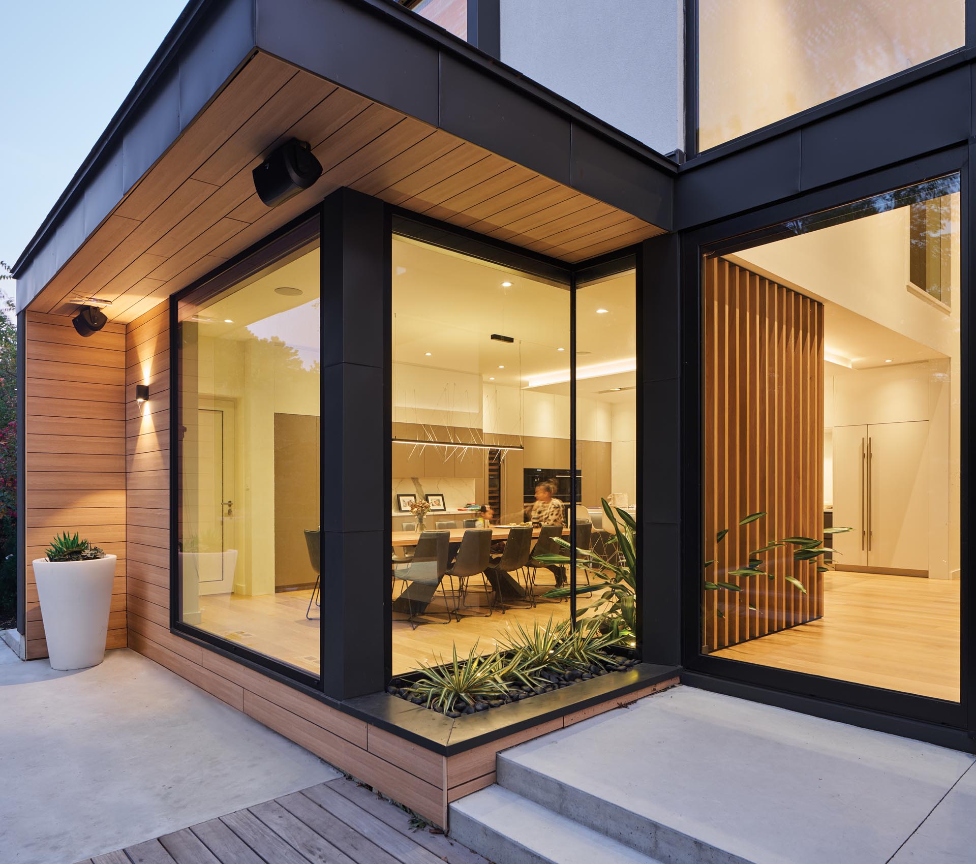 A modern house with a built-in planter, and black-framed windows and sliding glass doors.