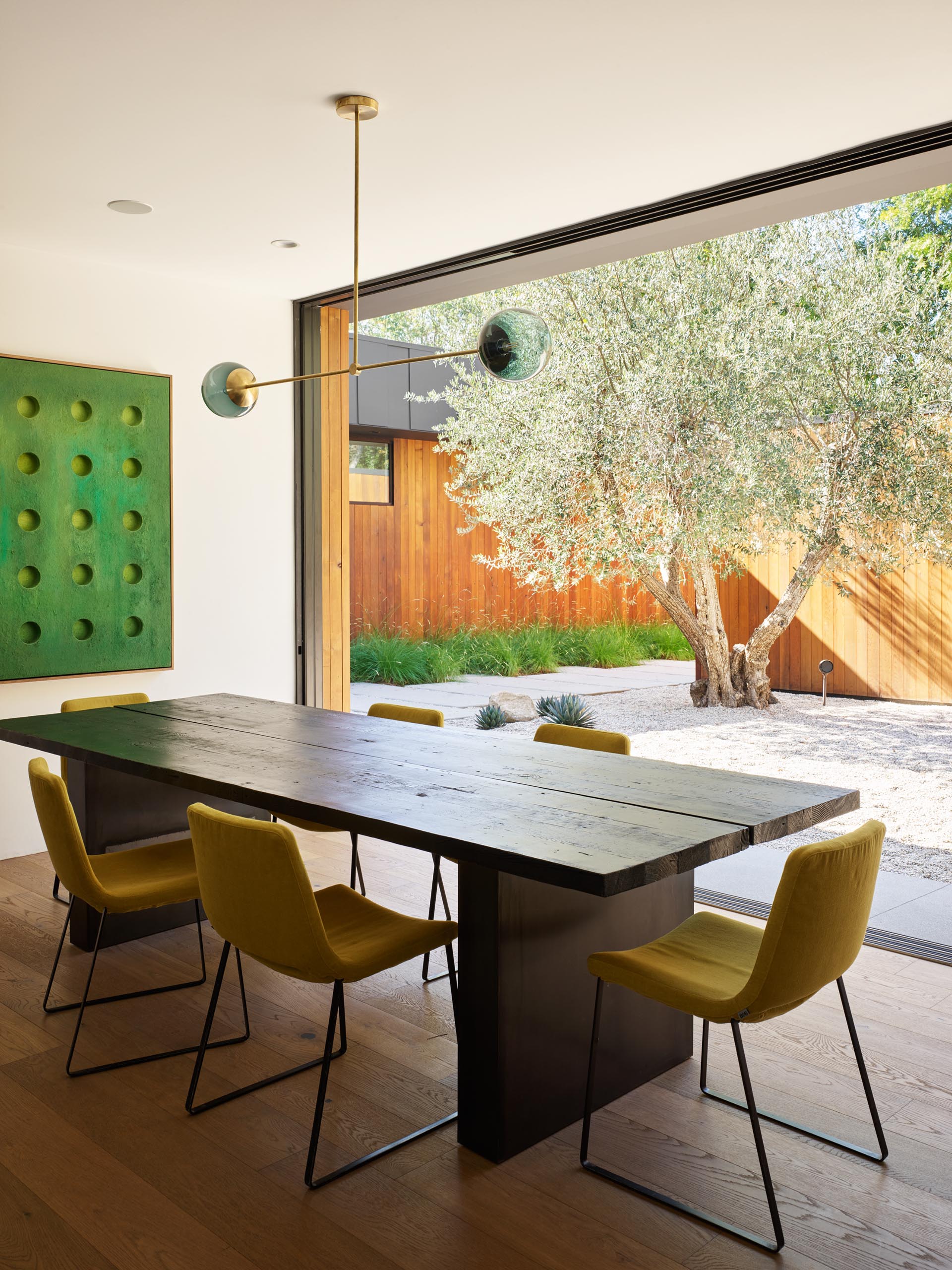 A modern dining room with a wood table, upholstered chairs, and sliding doors that open to a courtyar.