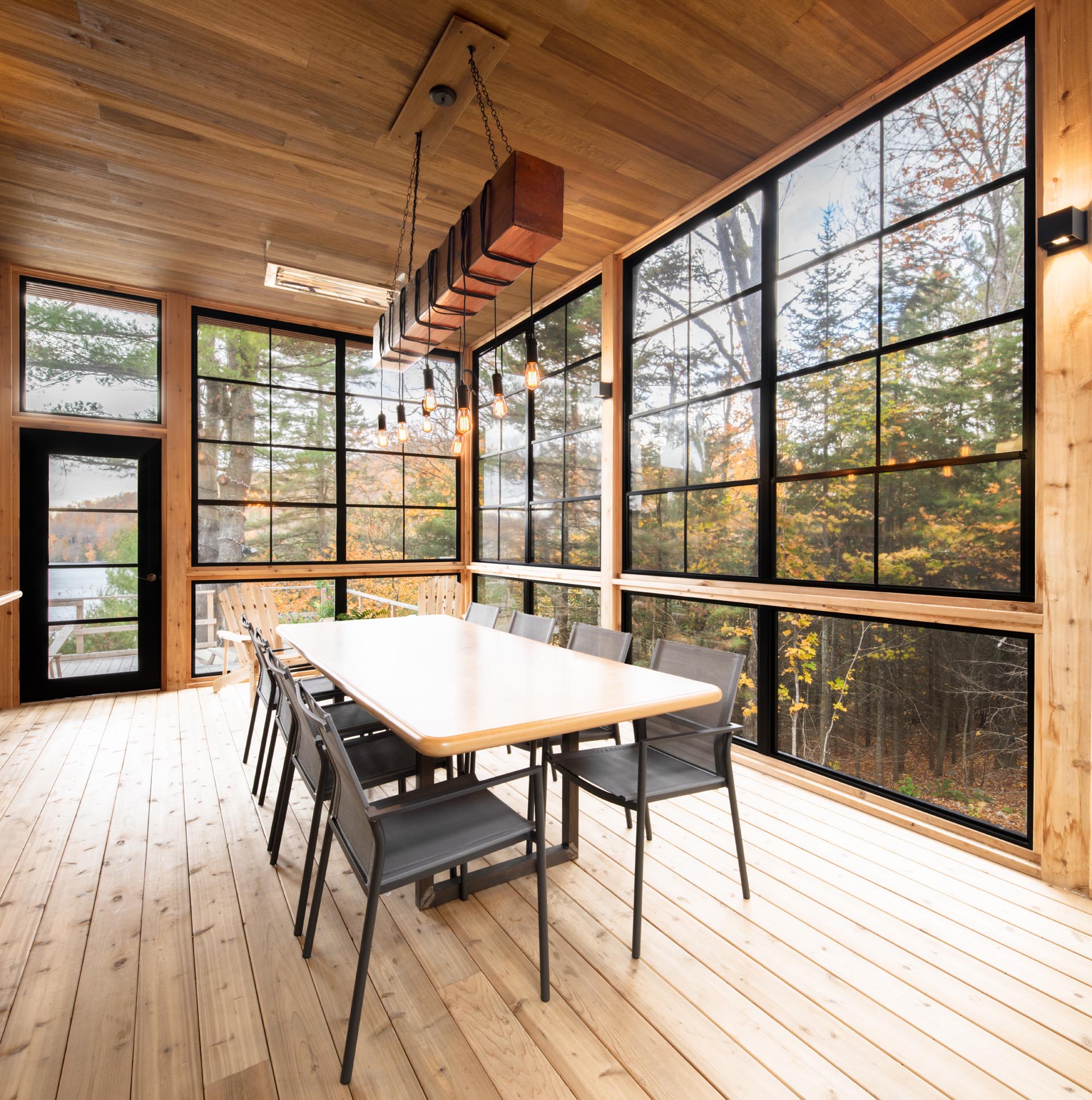 A screened-in porch with black-framed windows is furnished with a large dining table, perfect for group gatherings.