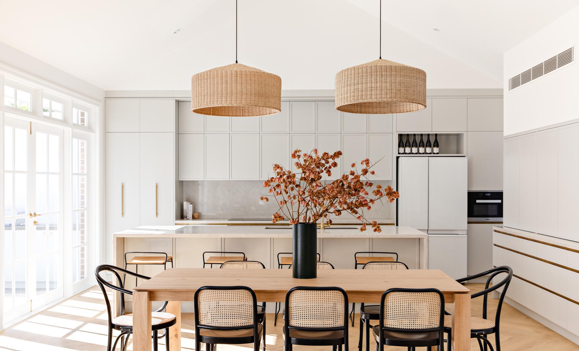 A modern dining area with a wood table, two woven pendant lights, and black-framed dining chairs.