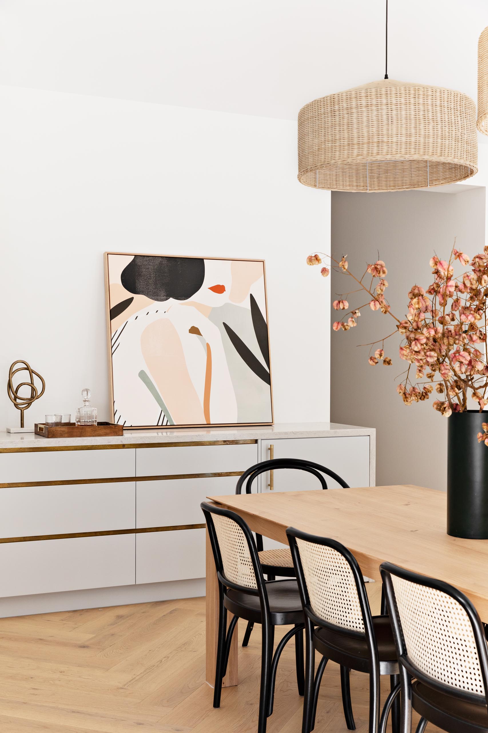 A modern dining area with a wood table, two woven pendant lights, and black-framed dining chairs.