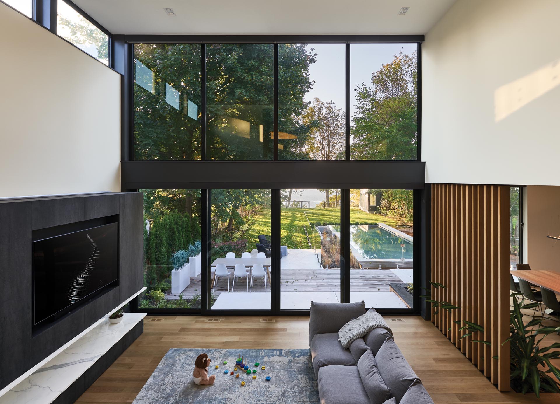 The interior of this modern house includes a double-height great room that has a wall of windows that look out to the swimming pool, yard, and lake views.