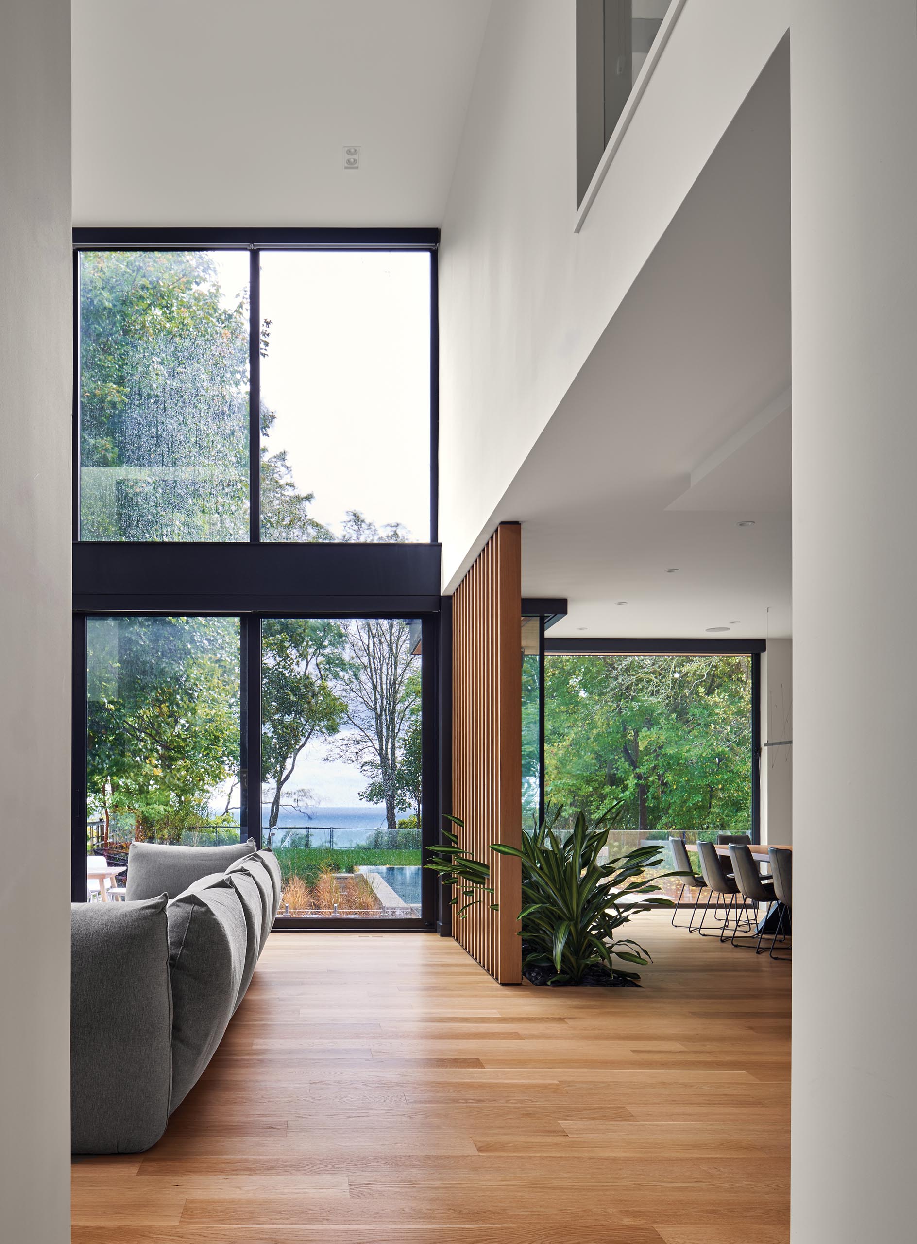 A modern house with double-height windows and ceiling, a wood slat partition, and a built-in planter.