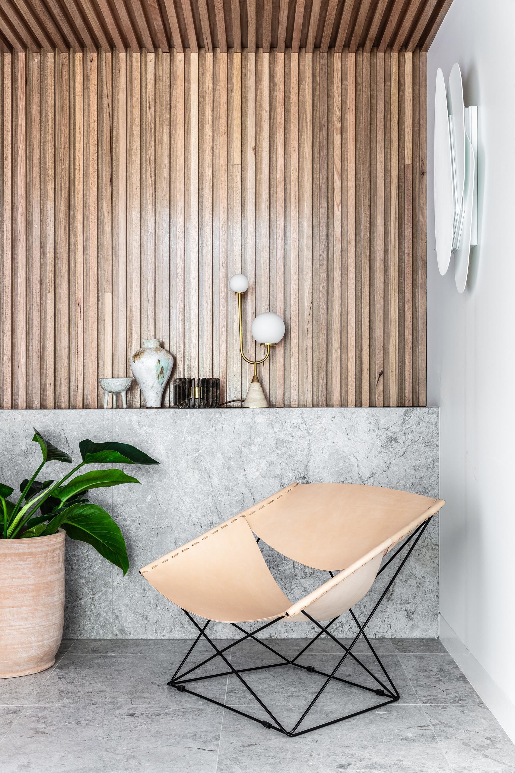 A modern entryway with a leather chair, a wood slat wall that flows onto the ceiling, and a stone accent that acts as a shelf.