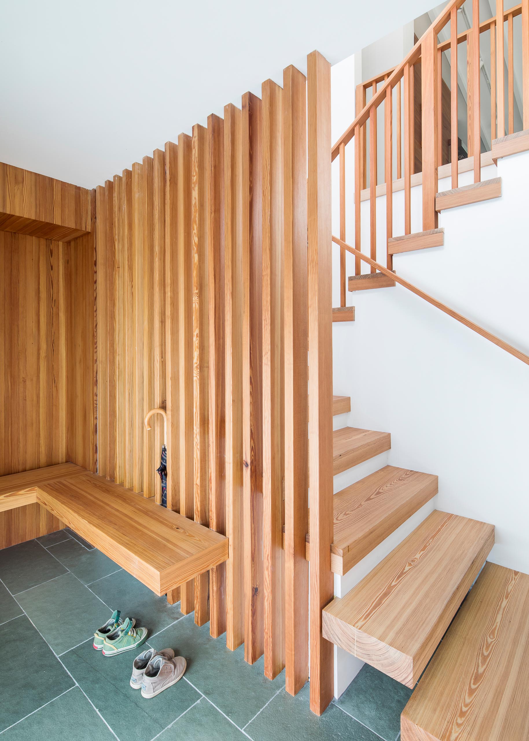 An entryway with a custom designed floating bench and wood slats that open up to the stairs that lead to the main social areas of the house.