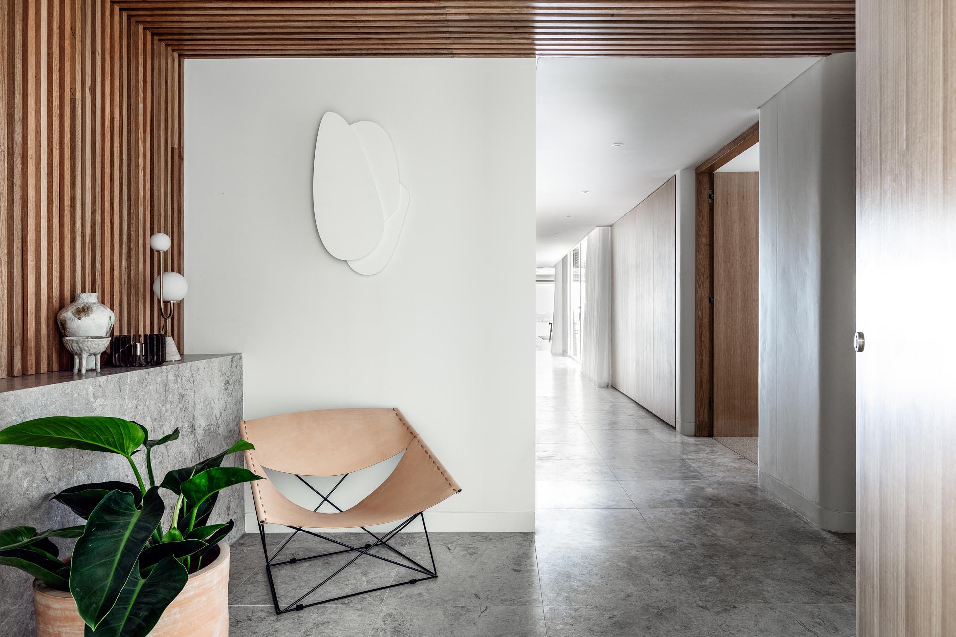 A modern entryway with a leather chair and wood slat wall that flows onto the ceiling.