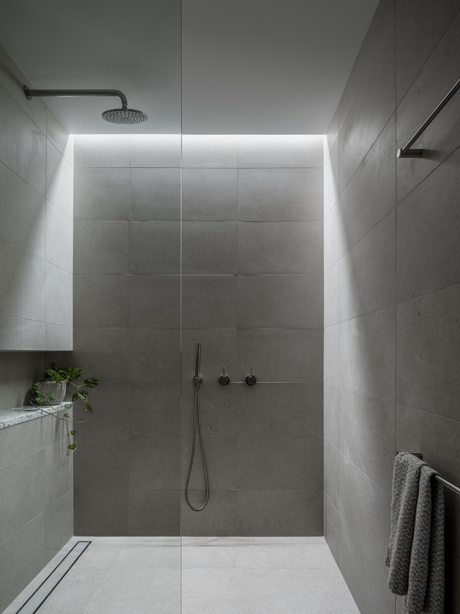 A gray tiled shower with a skylight, shower niche, and a linear drain.