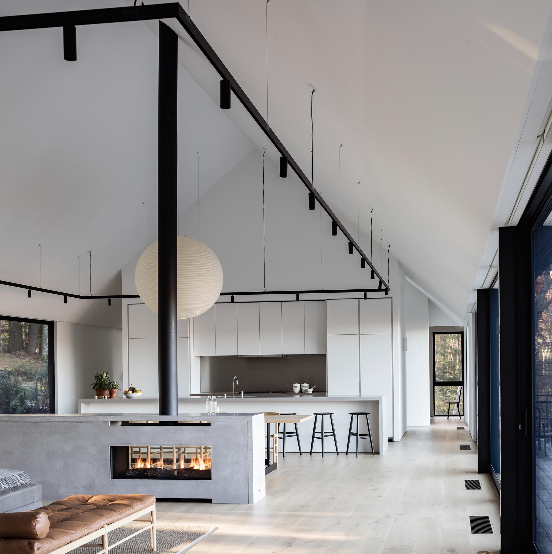 A modern house interior with a see-through fireplace, a minimalist white kitchen, and black accents.