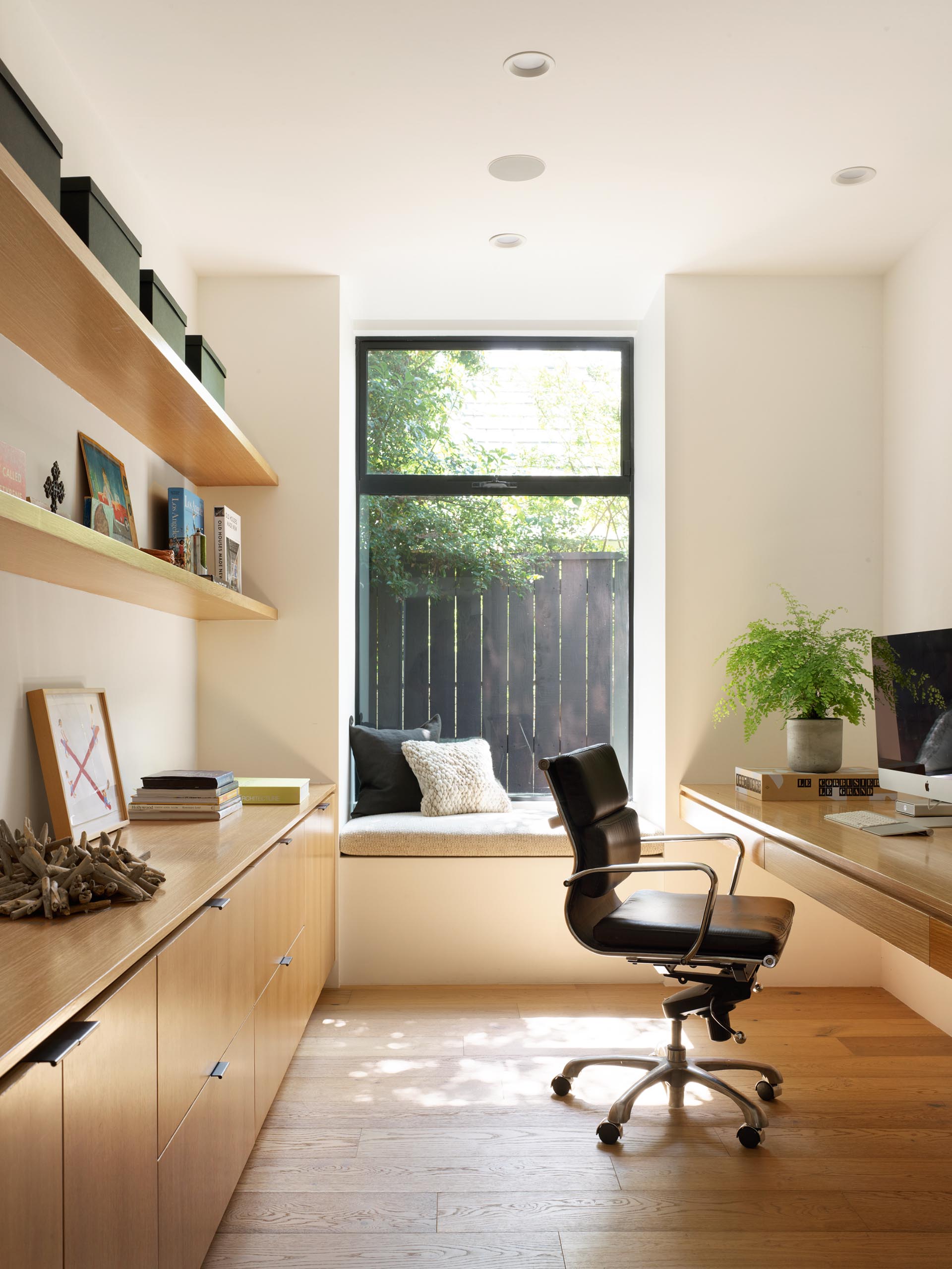 A home office furnished with a desk, a window seat, shelving, and cabinetry.