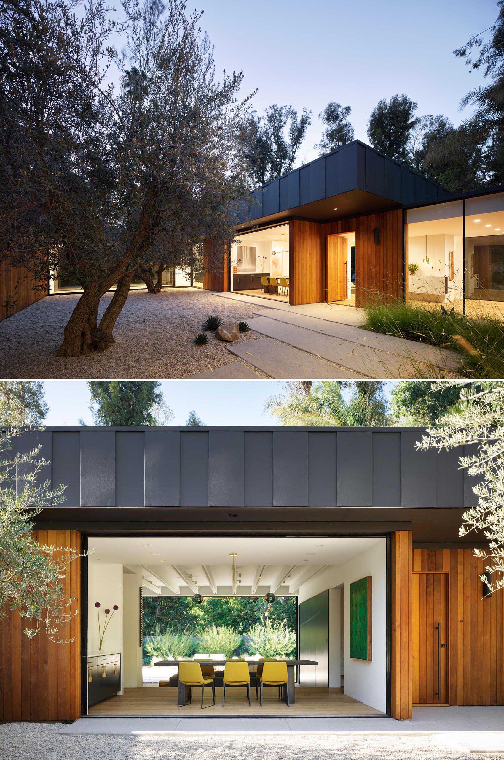 A walkway of concrete pavers lined by wild grasses lead visitors past a courtyard with olive trees and onto to the front door. 