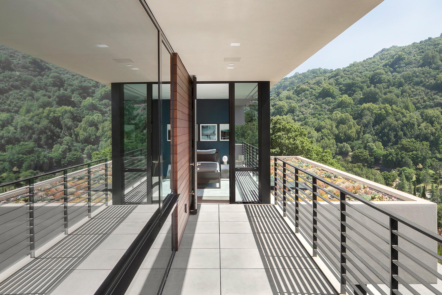 A bedroom opens up to a balcony with views of the surrounding hills and a green roof.