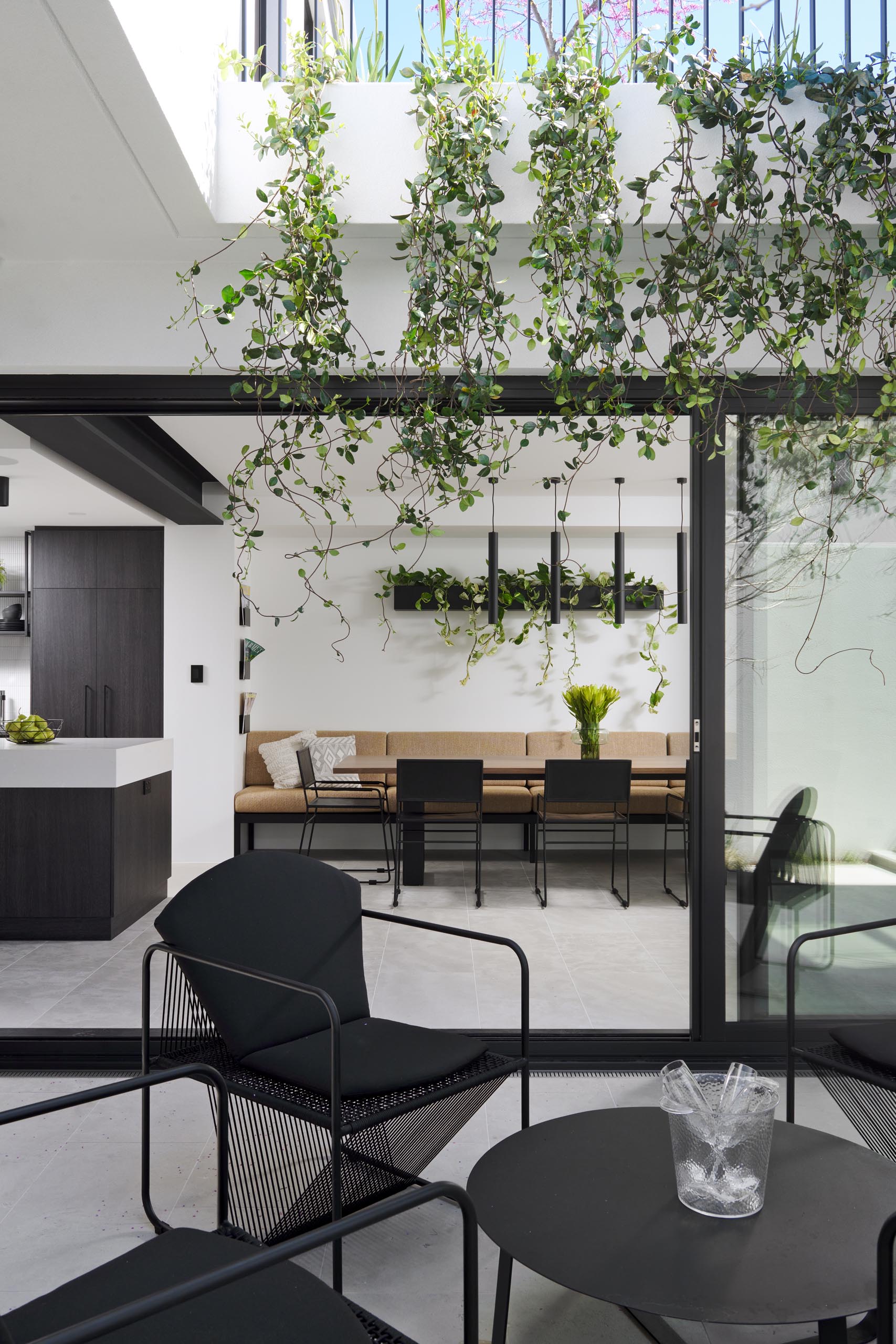 This modern dining room is adjacent to the kitchen and includes a long built-in banquette bench, a wall-mounted planter, and black dining chairs.