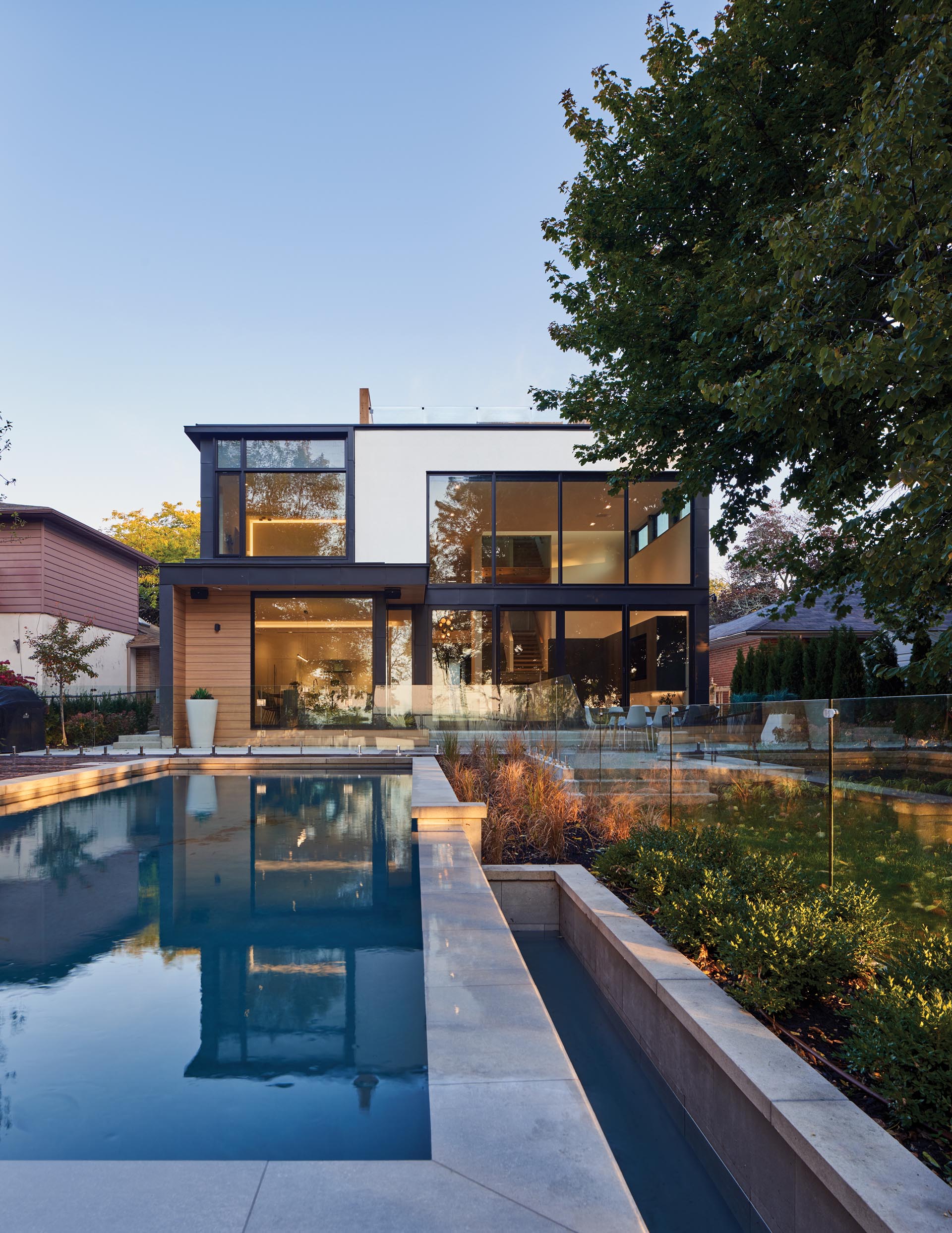 A modern house with double-height windows, a swimming pool, and a patio with room for outdoor dining.