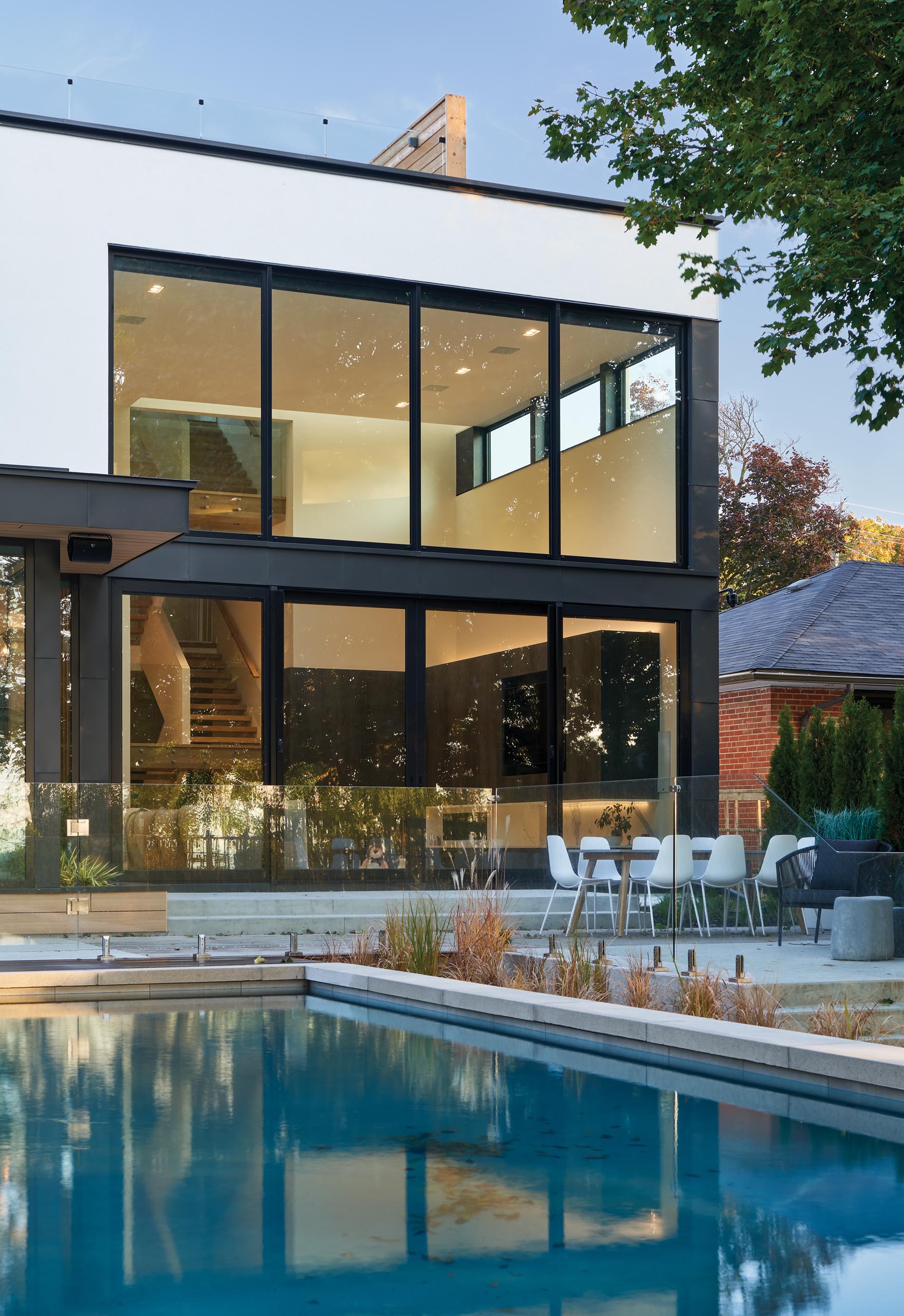 A modern house with double-height windows, a swimming pool, and a patio with room for outdoor dining.