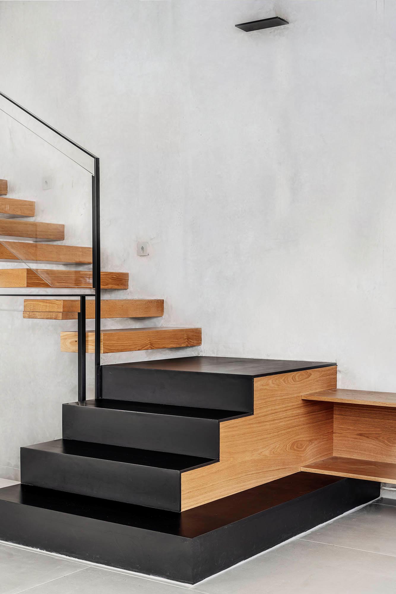 A floating oak staircase connects the various levels of this modern home, incorporates black iron stairs at the bottom, and transitions to become the TV sideboard in the living room.