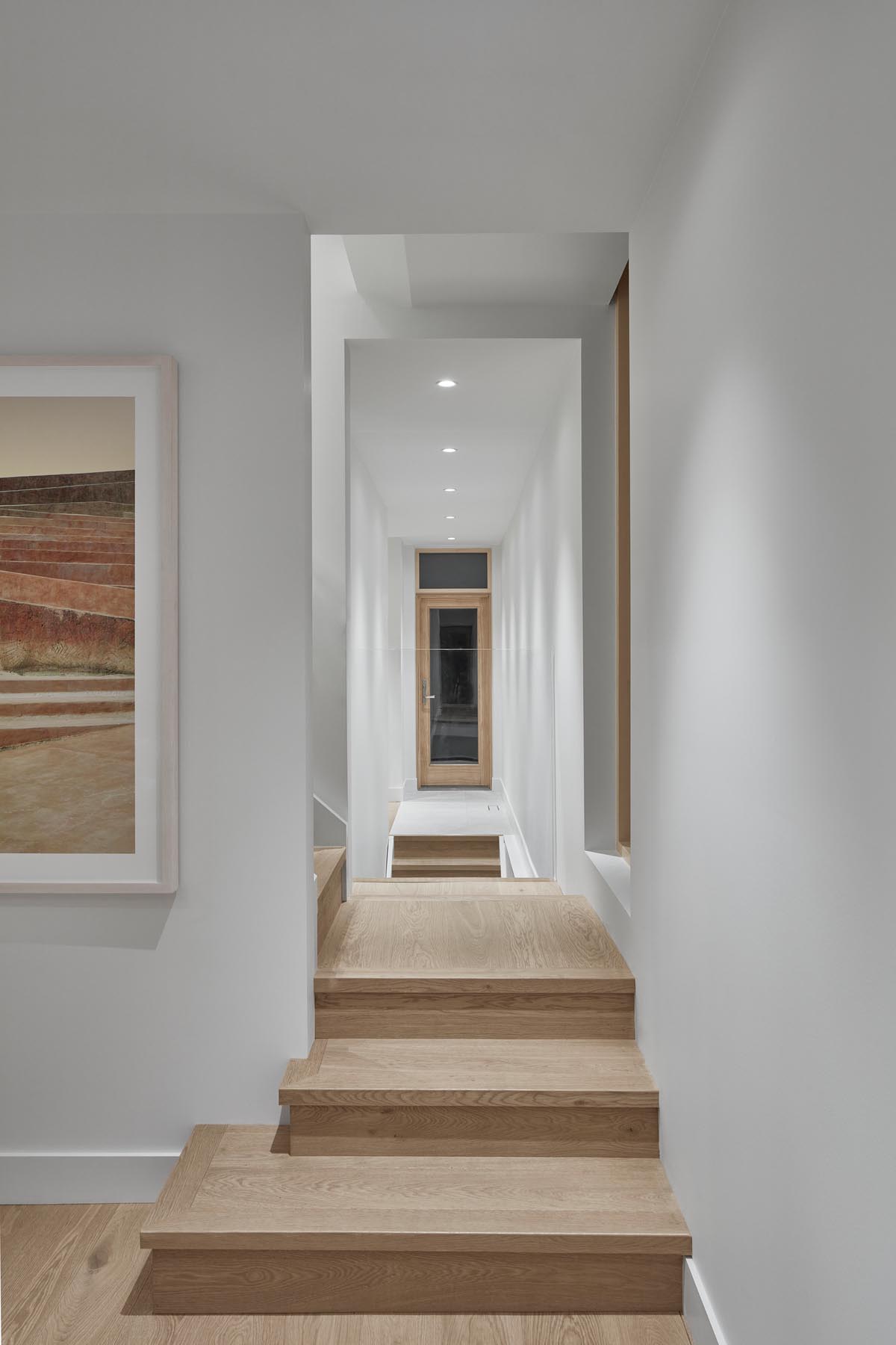 A modern hallway with wood floors, window frames, and doors.