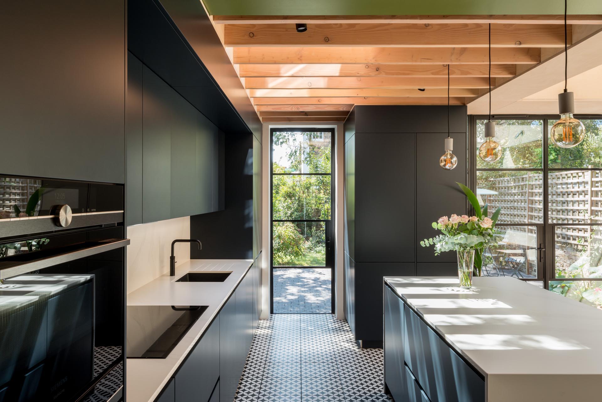 Minimalist matte black cabinets in this modern kitchen contrast the white countertops, while the patterned floor tile adds an artistic touch.