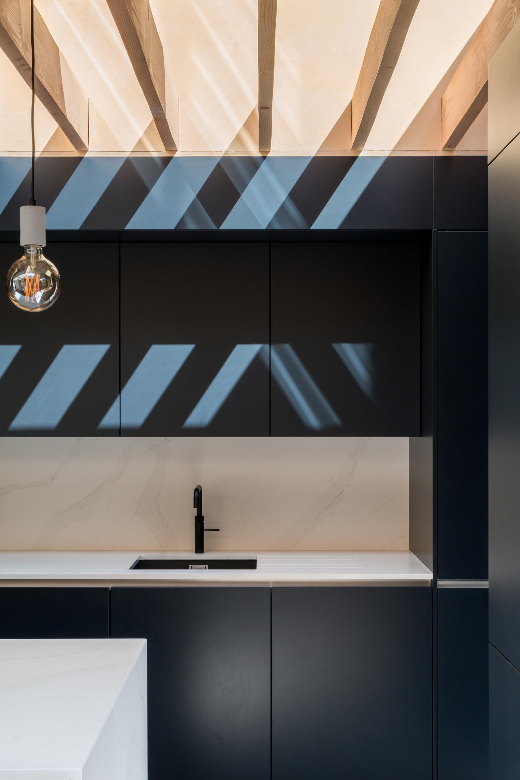 Modern matte black kitchen cabinets contrast the white countertops.