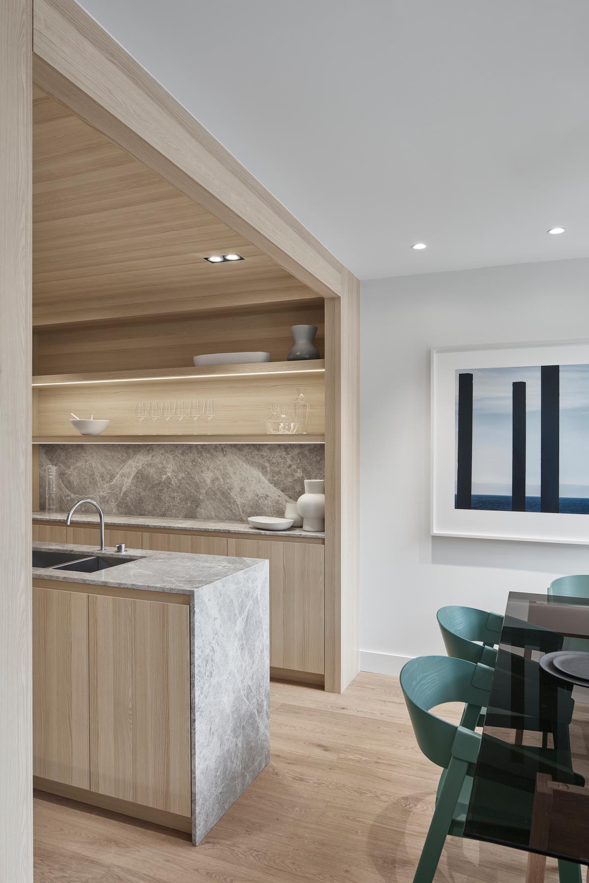 A modern kitchen with light wood cabinets, hidden lighting, and a long central island.